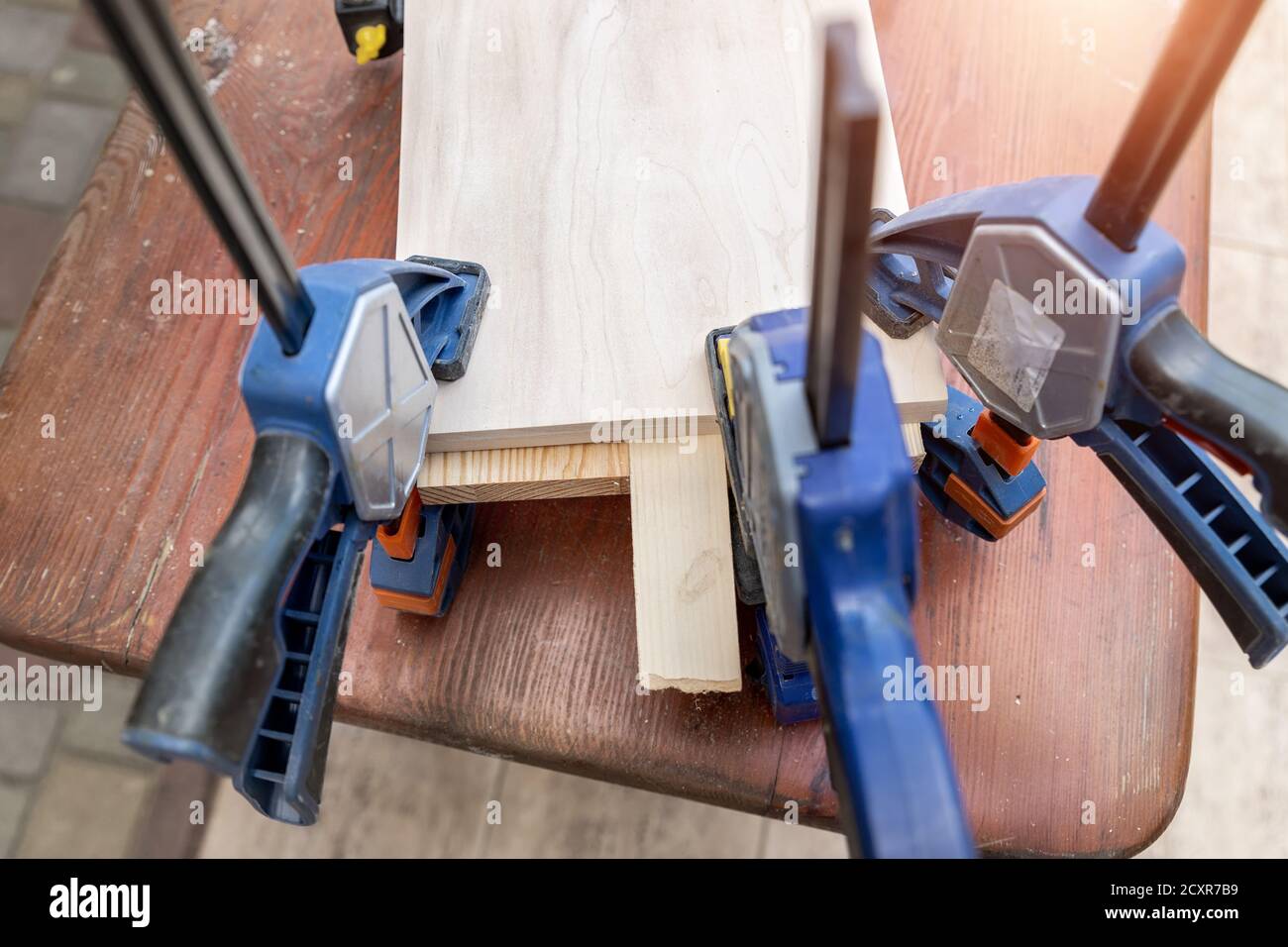 Joining wooden handmade box with clamps joiners after glueing. Different chisels, drills and pencils at craftsman workshop. DIY instruments on wood Stock Photo
