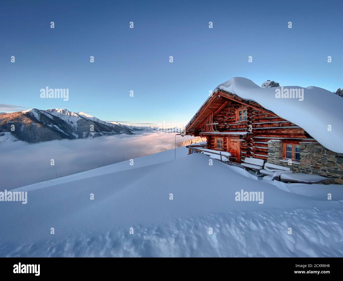 Snow covered mountain hut old farmhouse in the ski region of Saalbach Hinterglemm in the Austrian alps at sunrise against blue sky Stock Photo