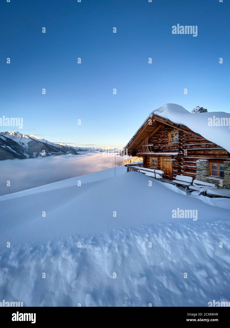 Snow covered mountain hut old farmhouse in the ski region of Saalbach Hinterglemm in the Austrian alps at sunrise against blue sky Stock Photo