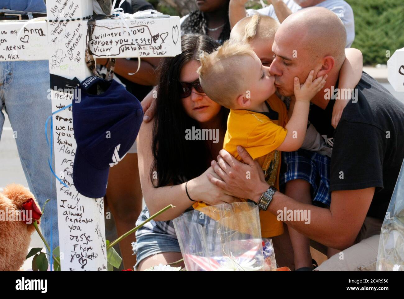 Trevor Dierecks (R) kisses his son Kameron next to his wife Rebecca (L) kneeling at a cross for Air Force Staff Sergeant Jesse Childress at a memorial near the movie theater where Childress and 11 other people where killed last Friday in Aurora, Colorado July 23, 2012. REUTERS/Rick Wilking (UNITED STATES - Tags: POLITICS DISASTER CRIME LAW) Stock Photo