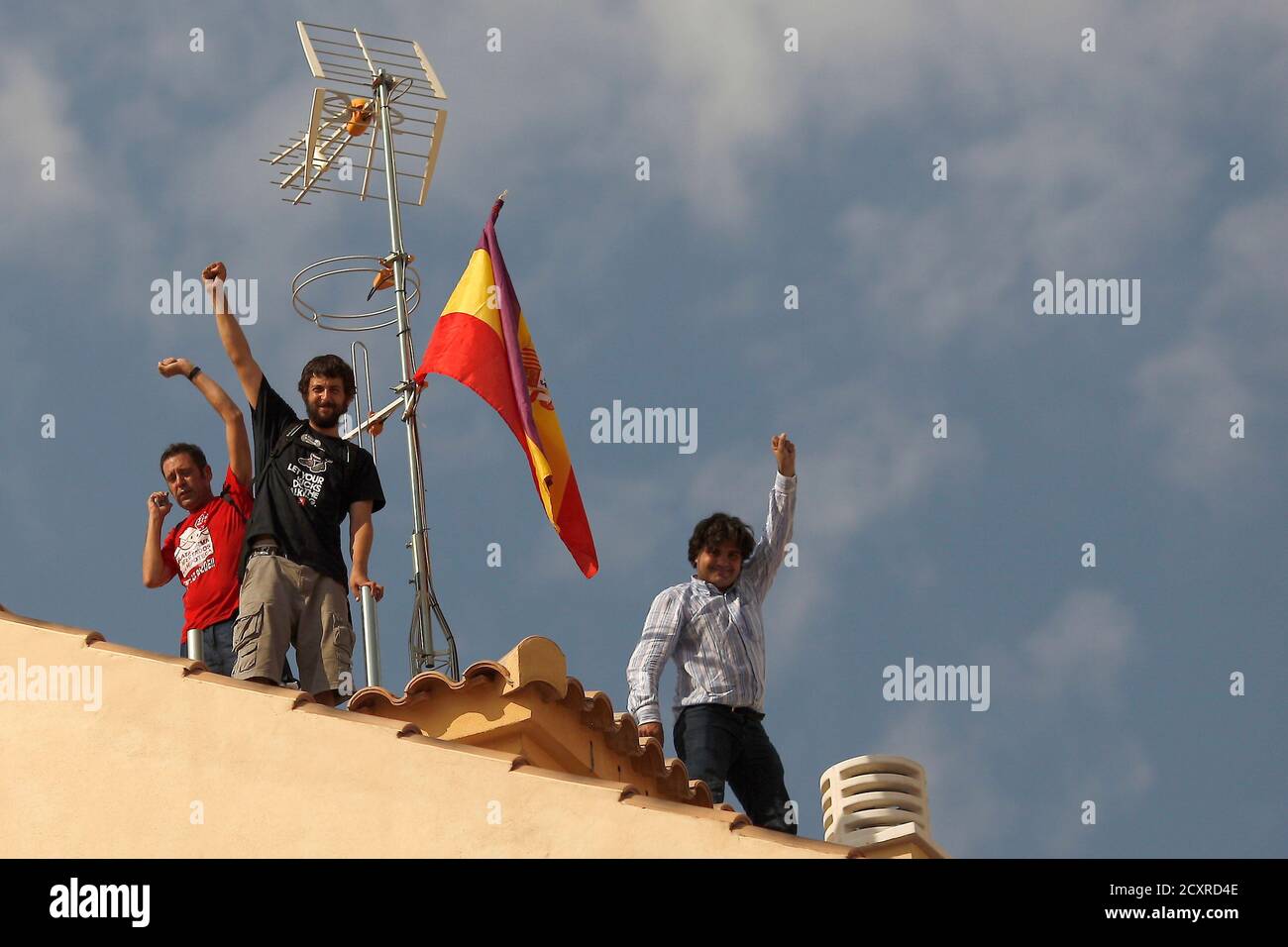 Activists raise their fists next to a Spanish Republican era flag on a roof after Spanish riot police evicted several families of an unoccupied building of flats in Malaga, southern Spain October 3, 2013. A total of 13 families, included 12 children, had occupied the building since February. Members from various support platforms failed to stop the eviction and three activists were arrested when they refused to leave the roof of building, according to local media. REUTERS/Jon Nazca (SPAIN - Tags: CIVIL UNREST POLITICS BUSINESS REAL ESTATE SOCIETY) Stock Photo