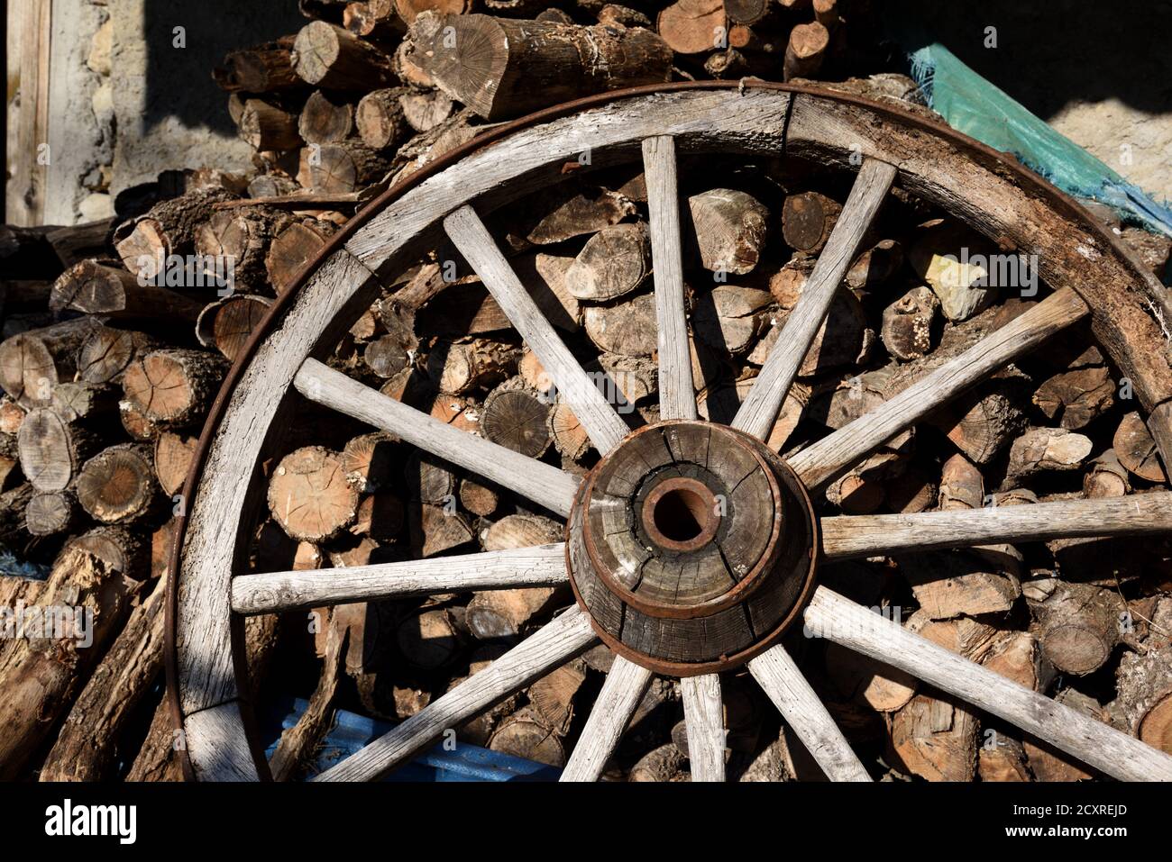 Old Wooden Cartwheel with Reinforced Wooden Hub & Wooden Spokes & Chopped Firewood Stock Photo