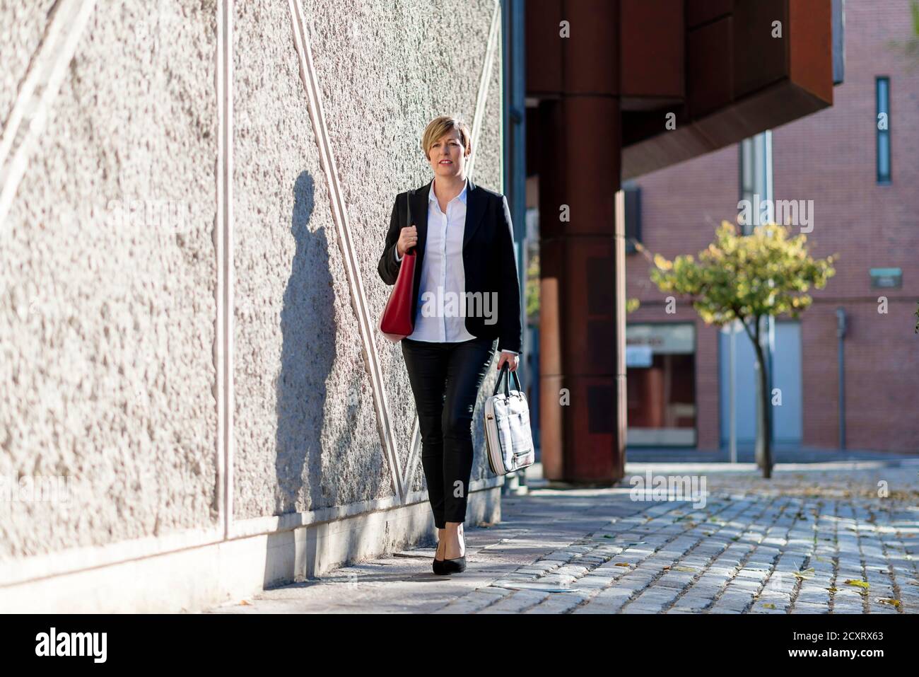 Woman walking with a laptop's bag next to office building Stock Photo