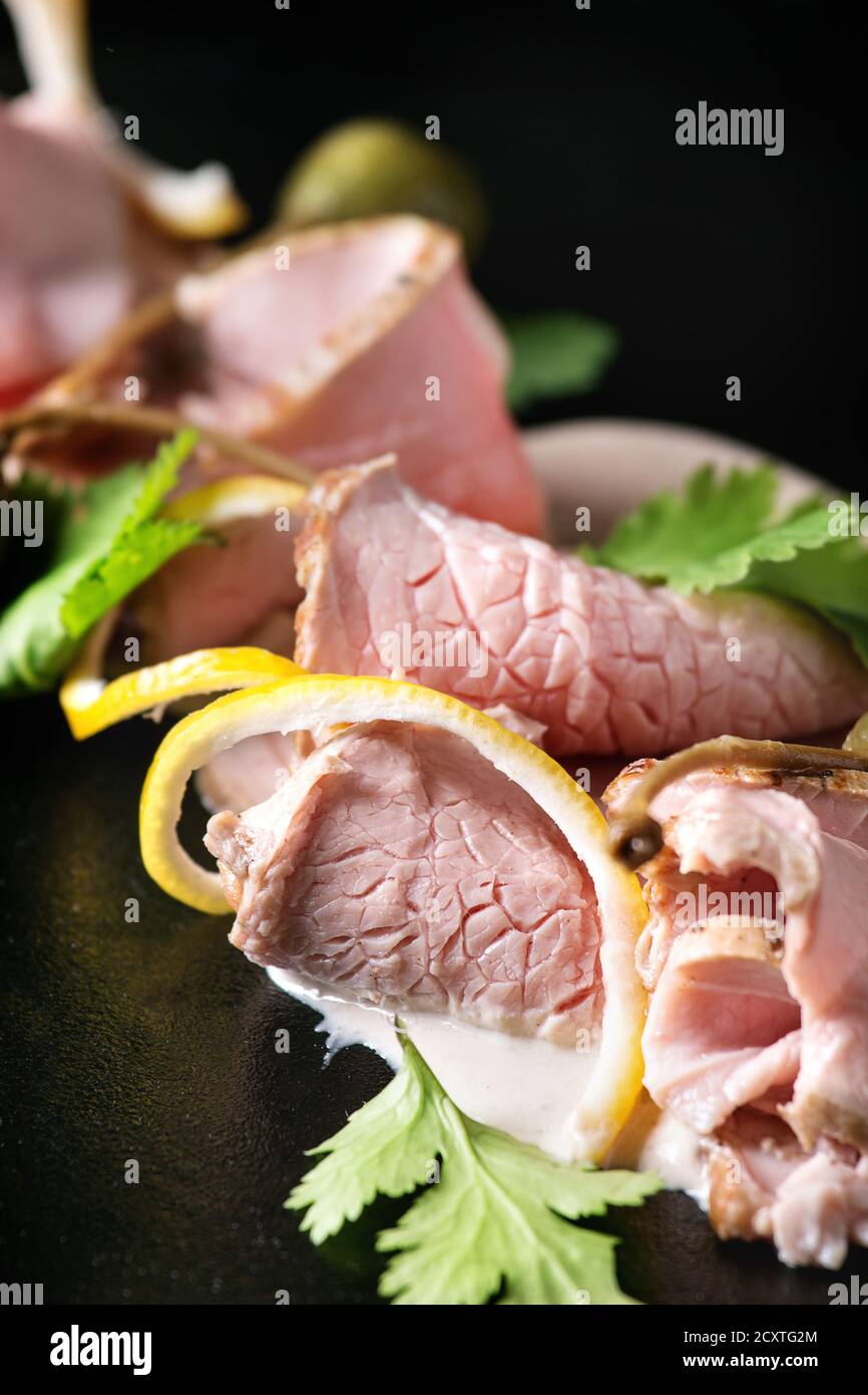 Vitello tonnato italian dish. Thin sliced veal with tuna sauce, capers and coriander served on black plate. Close up Stock Photo