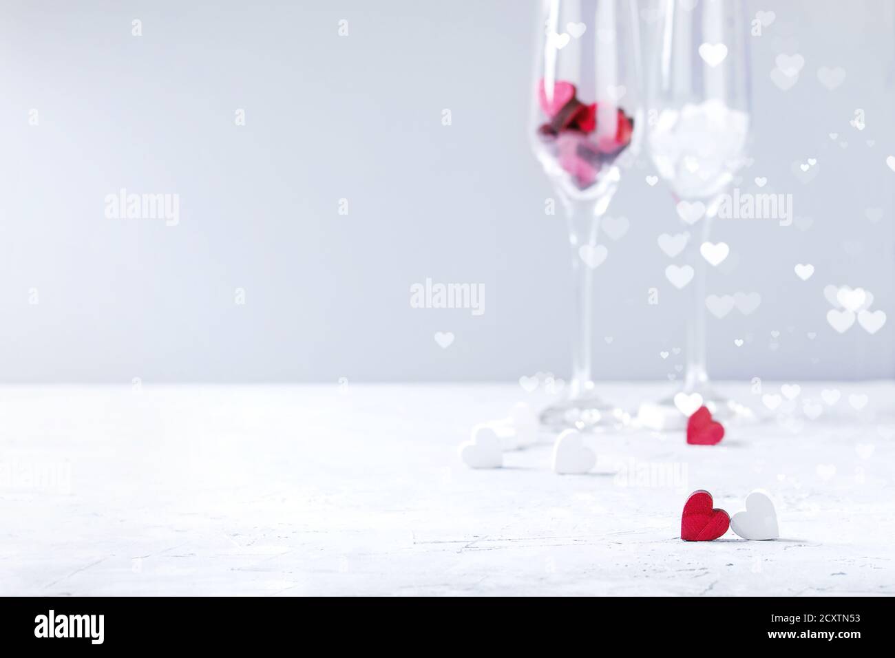 Love Valentine day greeting card with two empty champagne glasses and wooden hearts over white gray background. Copy space. Selective focus Stock Photo