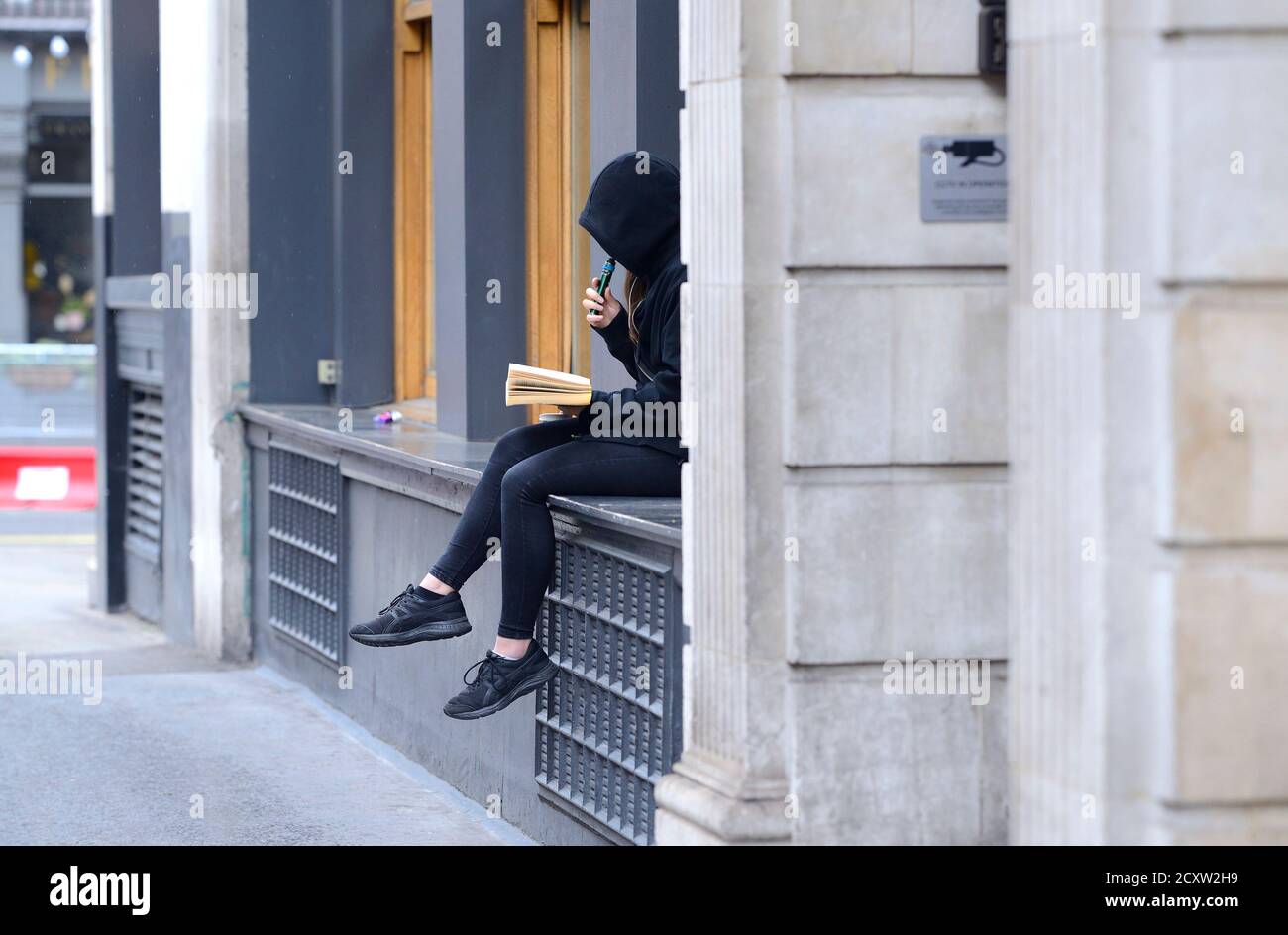 London, England, UK. Young woman reading a book and vaping in Covent Garden Stock Photo