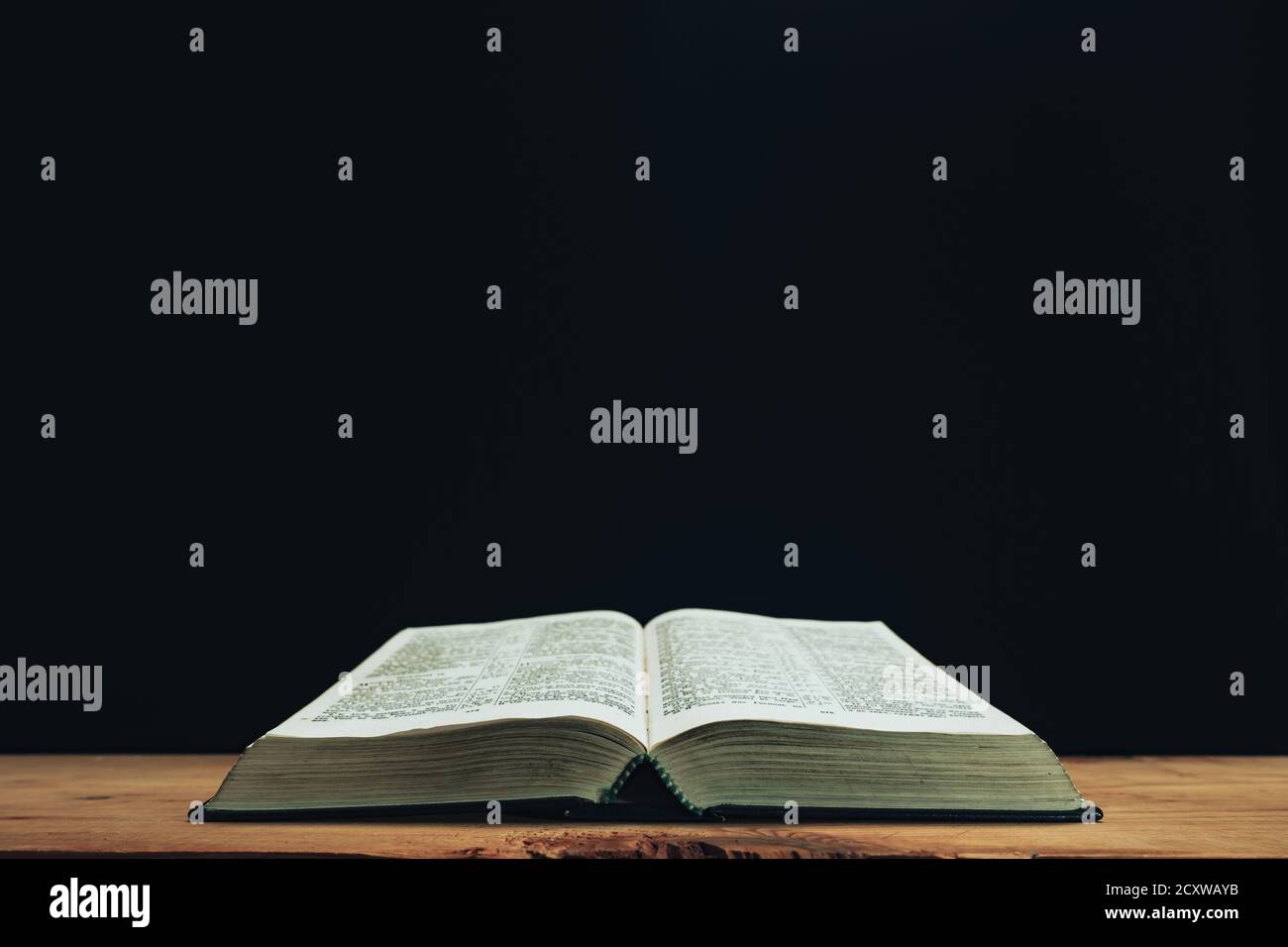 Open Holy Bible on a red old wooden table. Beautiful Black wall background. Stock Photo