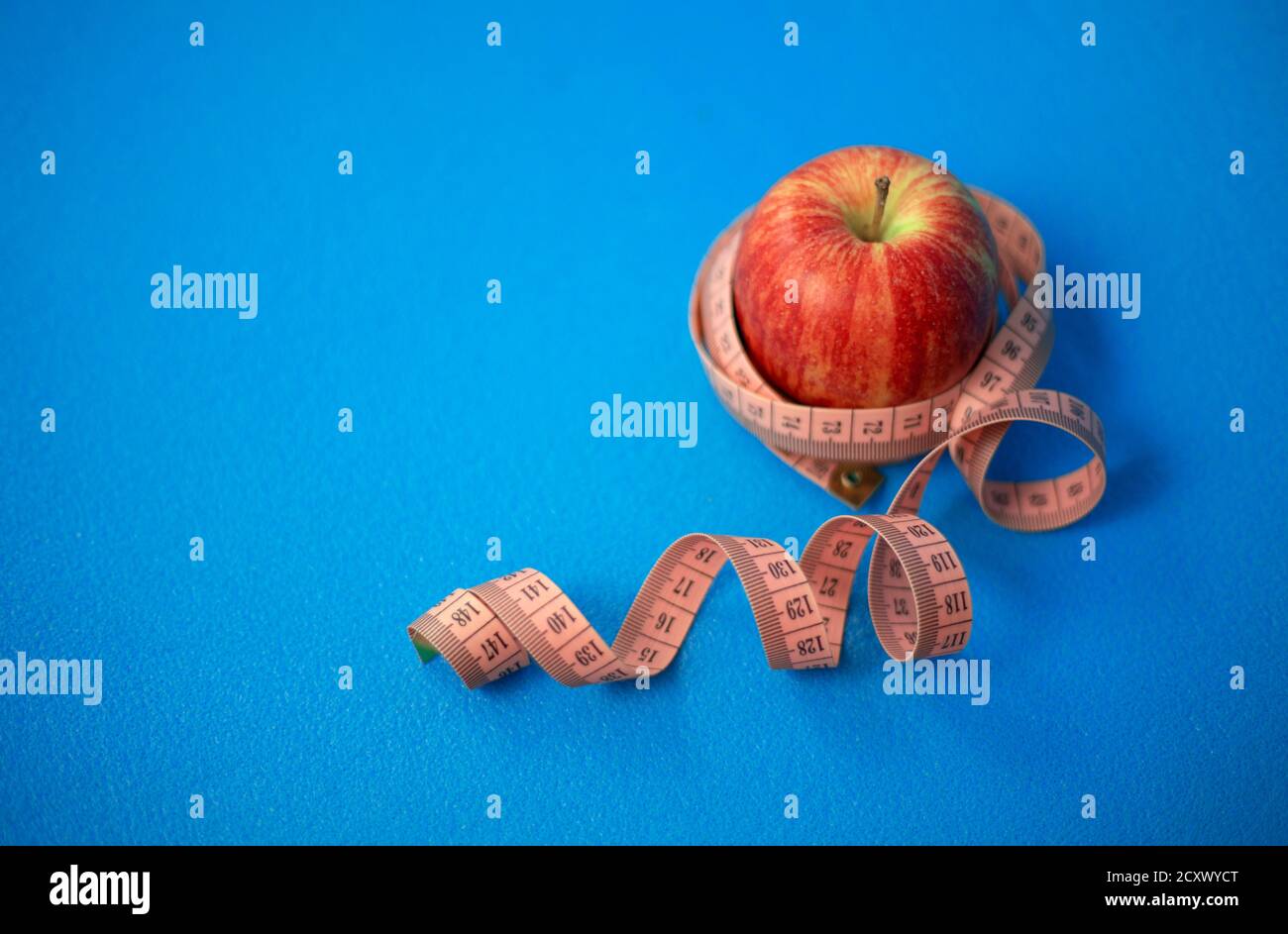 One apple a day for your health. Red apple with centimeter tape on a blue background. Stock Photo