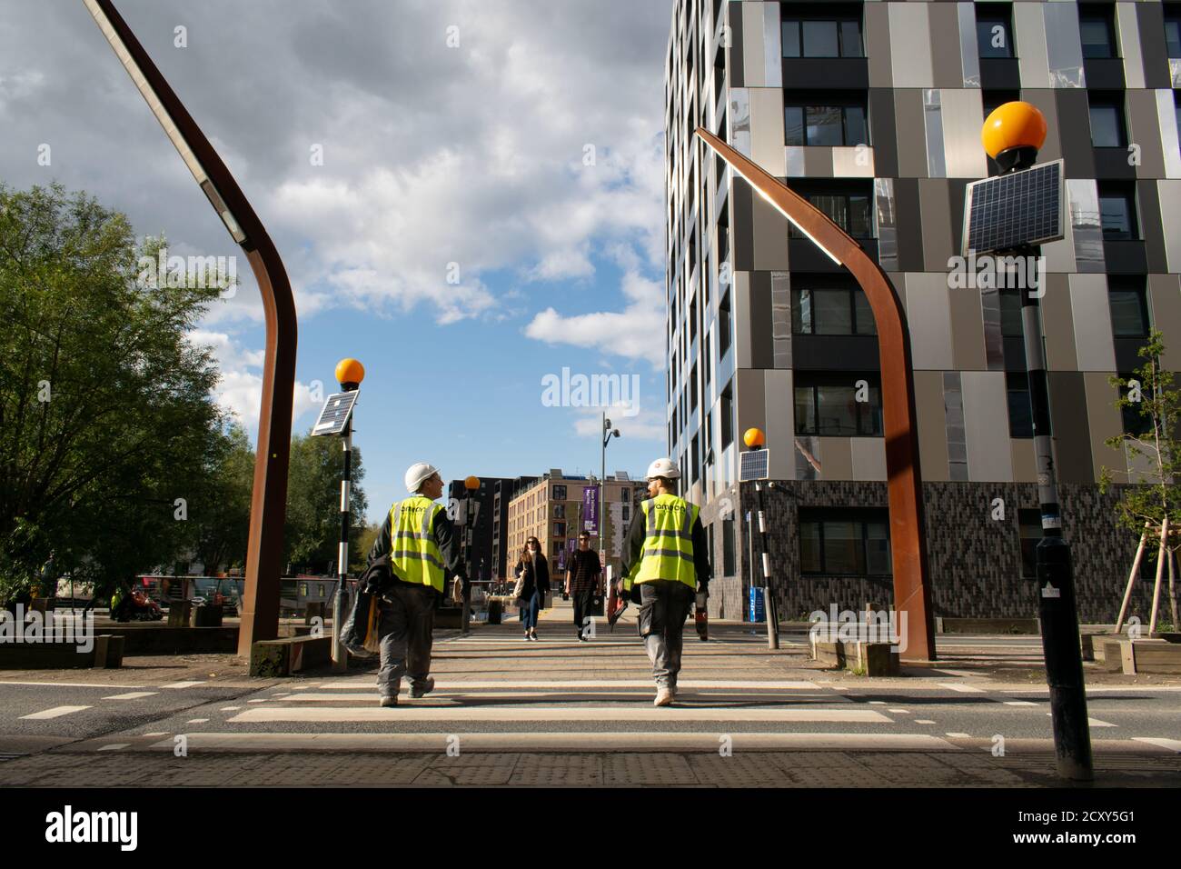 Construction workers walk across zebra crossing Old Mill Street leading to New Islington marina, Manchester UK. . Weavers Quay apartments Stock Photo