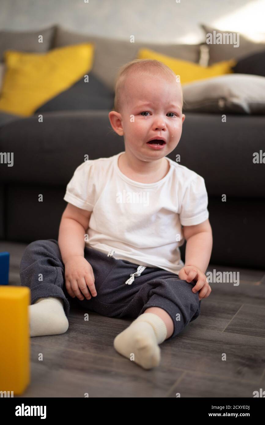 Little unhappy baby crying on the floor in his room Stock Photo