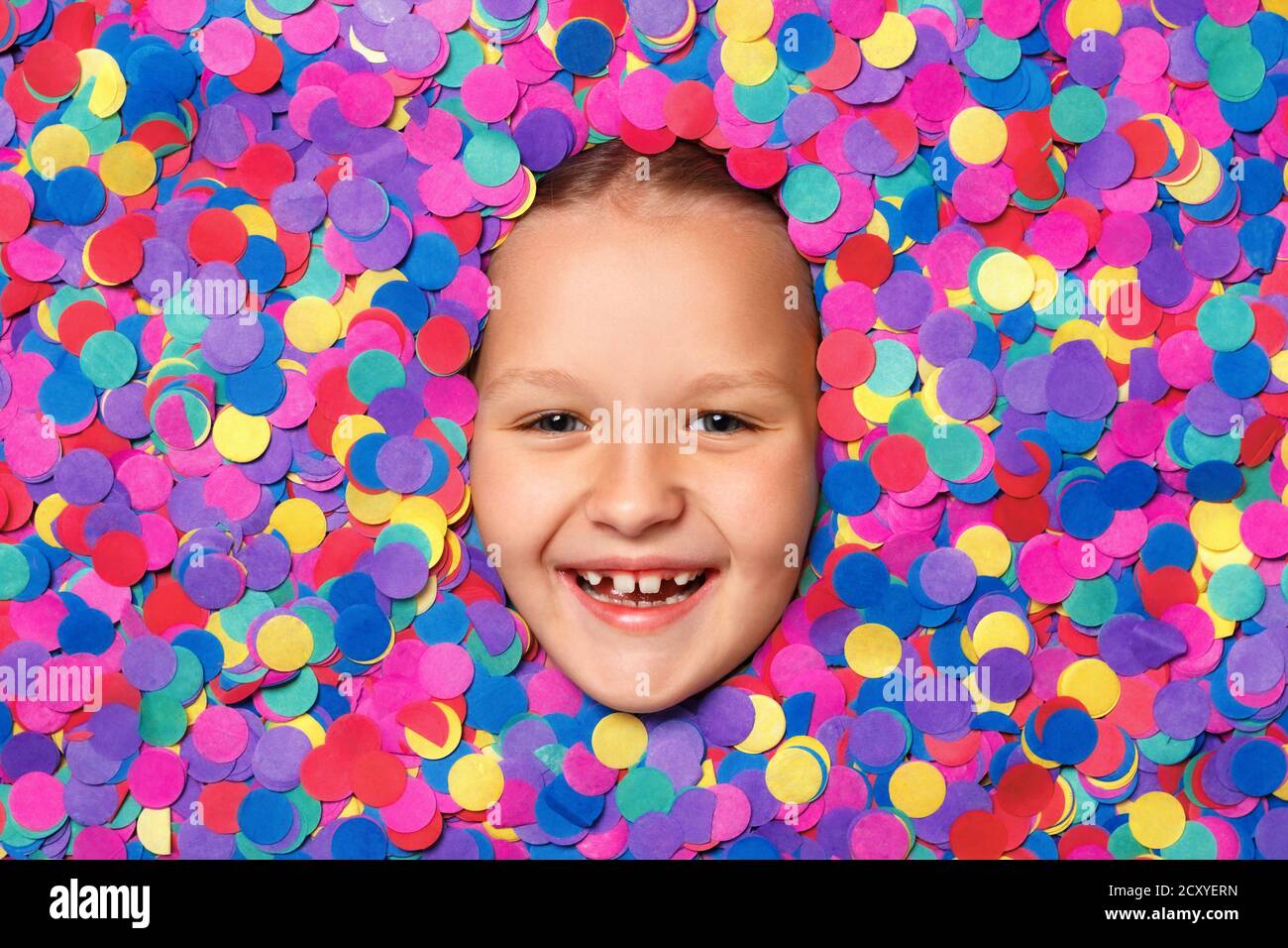 Cheerful cute little girl face in multicolored confetti. Top view of