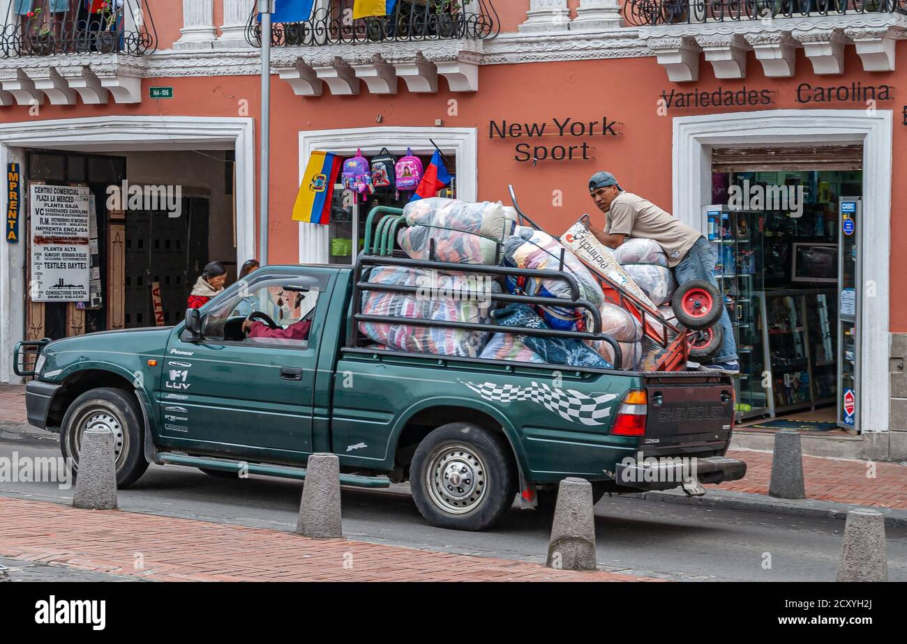 Quito, Ecuador - December 2, 2008: Historic downtown. Green pickup truck overloaded with plastic bags full of textiles delivers to New York Sport stor Stock Photo