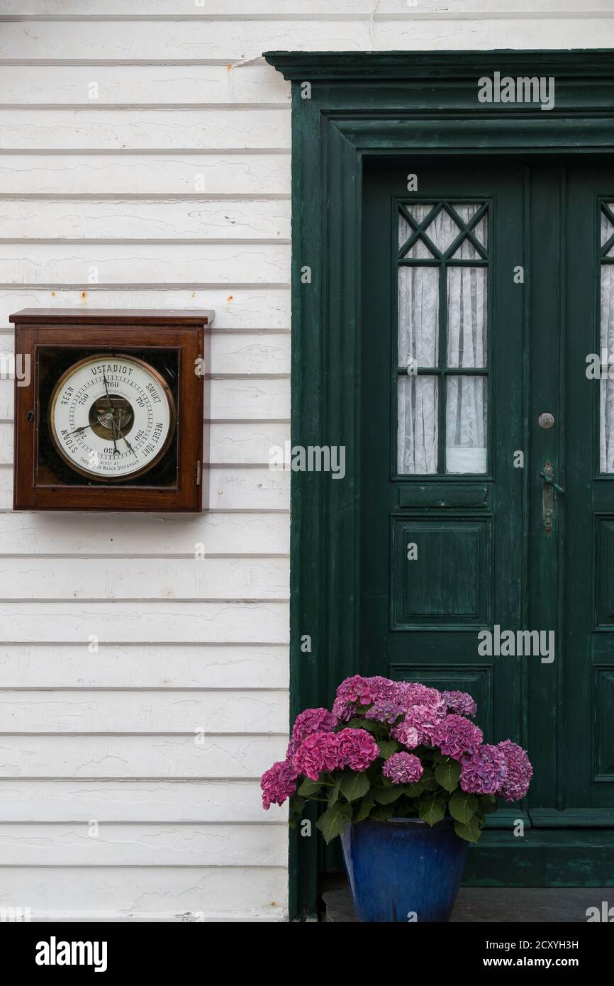 SKUDENESHAVN, NORWAY - 2018 JULY 05. Beautiful cosy entrance with flowers and a atmospheric weather pressure outside on the wall. Stock Photo