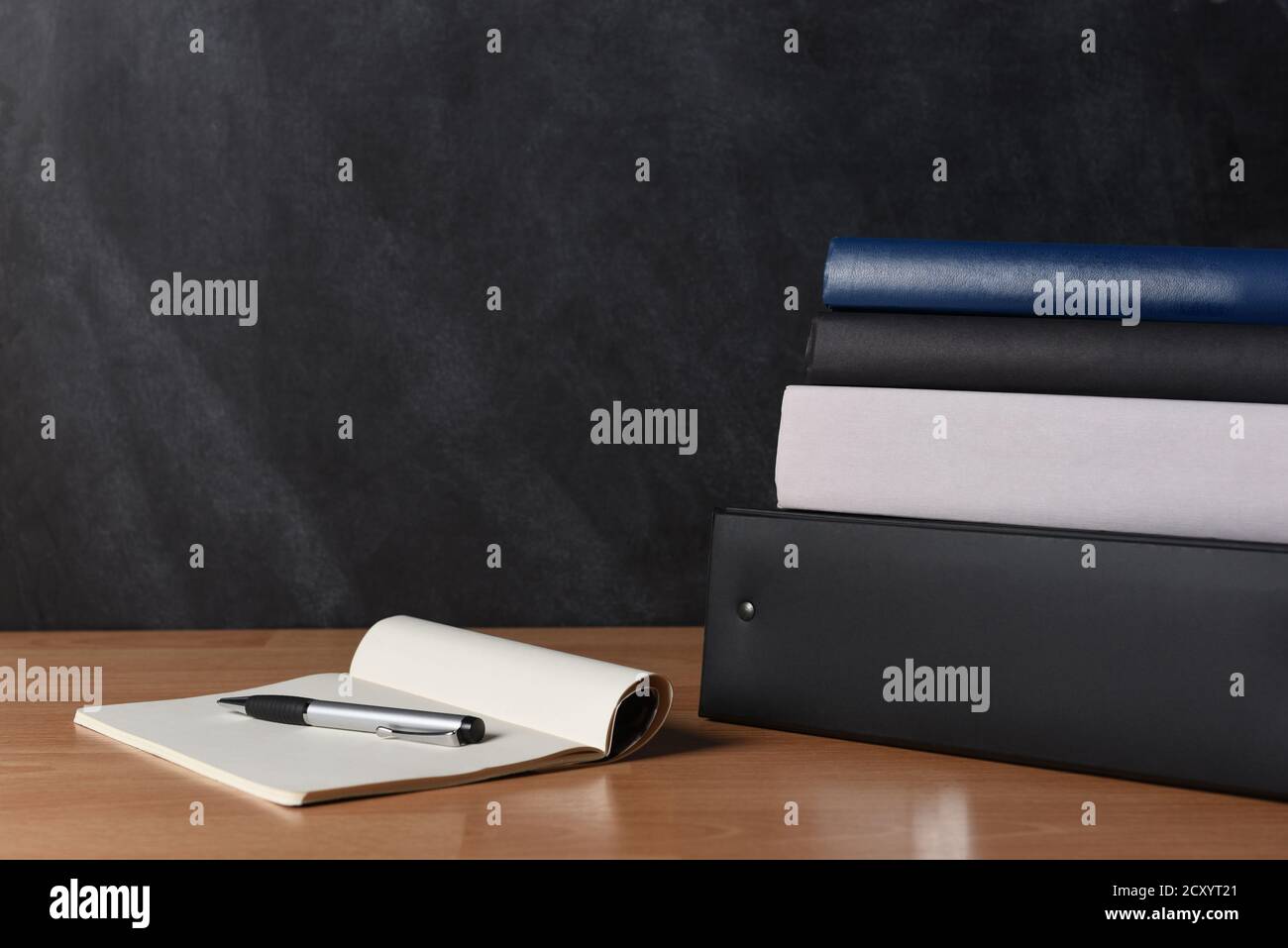 Teachers desk with note pad and pen and a stack of binders and books ...