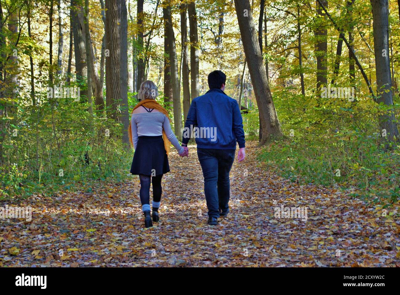 A young couple walking down a trail in the woods holding hands in the ...