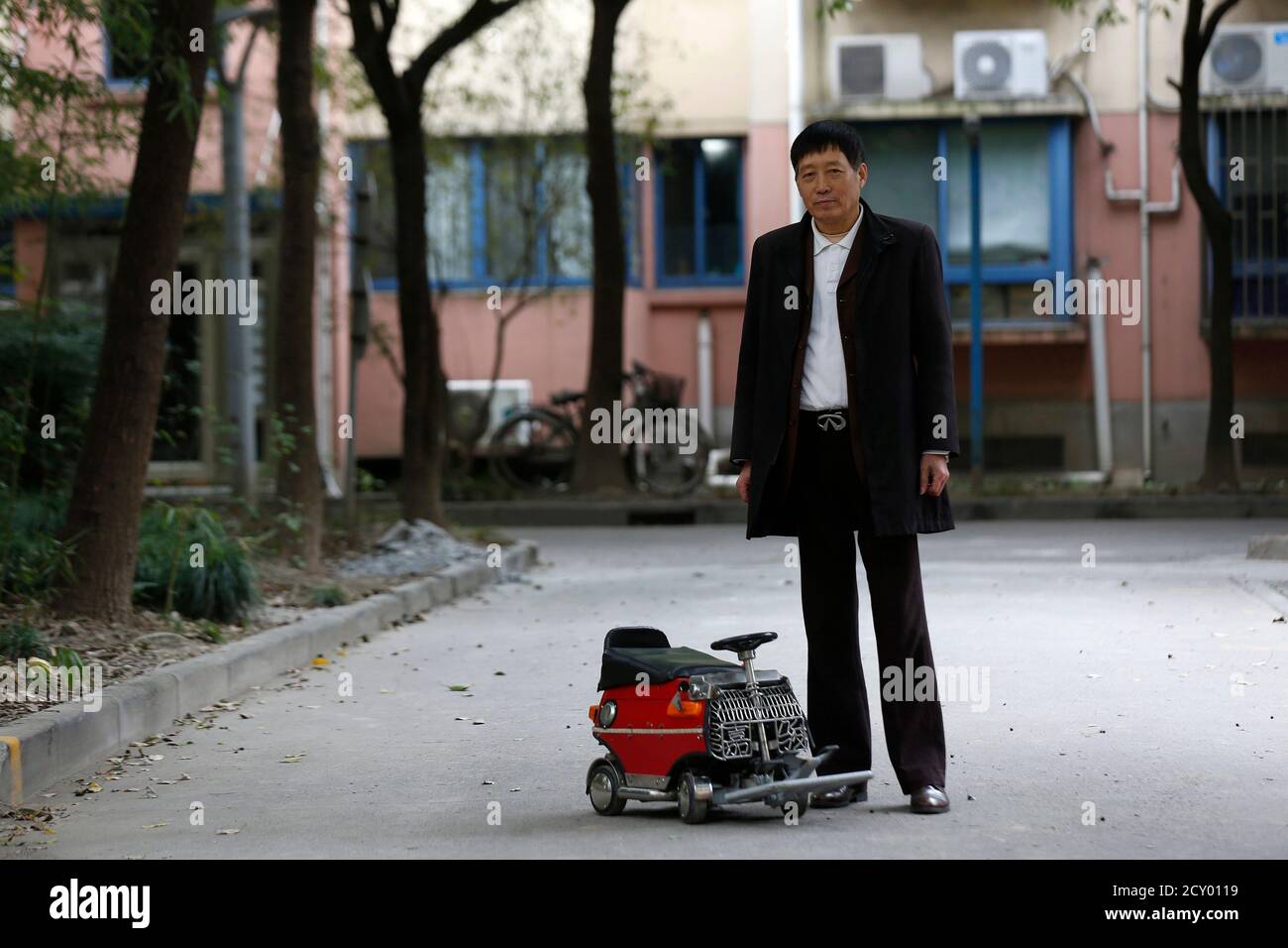 Xu Zhiyun, 60, poses with his home-made motorised mini-vehicle at a street in Shanghai December 9, 2014. Xu spent over two years to complete the mini-vehicle measuring 60cm (24 inches) by 35cm (14 inches) by 40cm (16 inches), which has a 77cc engine and five gear ranges. REUTERS/Aly Song  (CHINA - Tags: SOCIETY TRANSPORT) Stock Photo