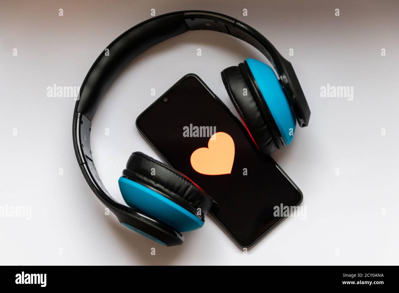 Black smartphone with red heart on the black screen and a cordless blue over ear headphone show mobile music streaming, health control and smartphone Stock Photo