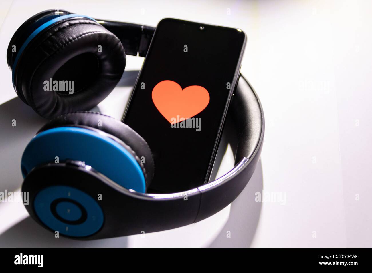 Black smartphone with red heart on the black screen and a cordless blue over ear headphone show mobile music streaming, health control and smartphone Stock Photo