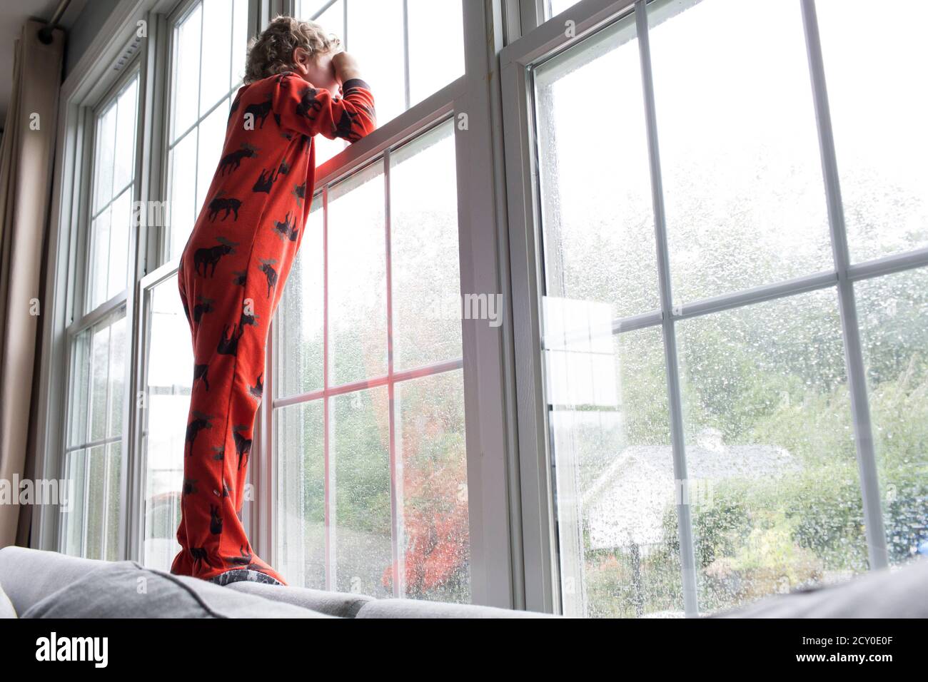 Low Angle View of Young Boy in Red Pajamas Looking Out Rainy Window