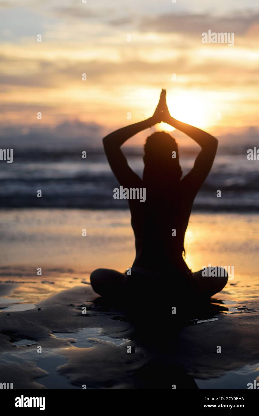 Silhouette of woman doing yoga on the beach at sunset Stock Photo - Alamy