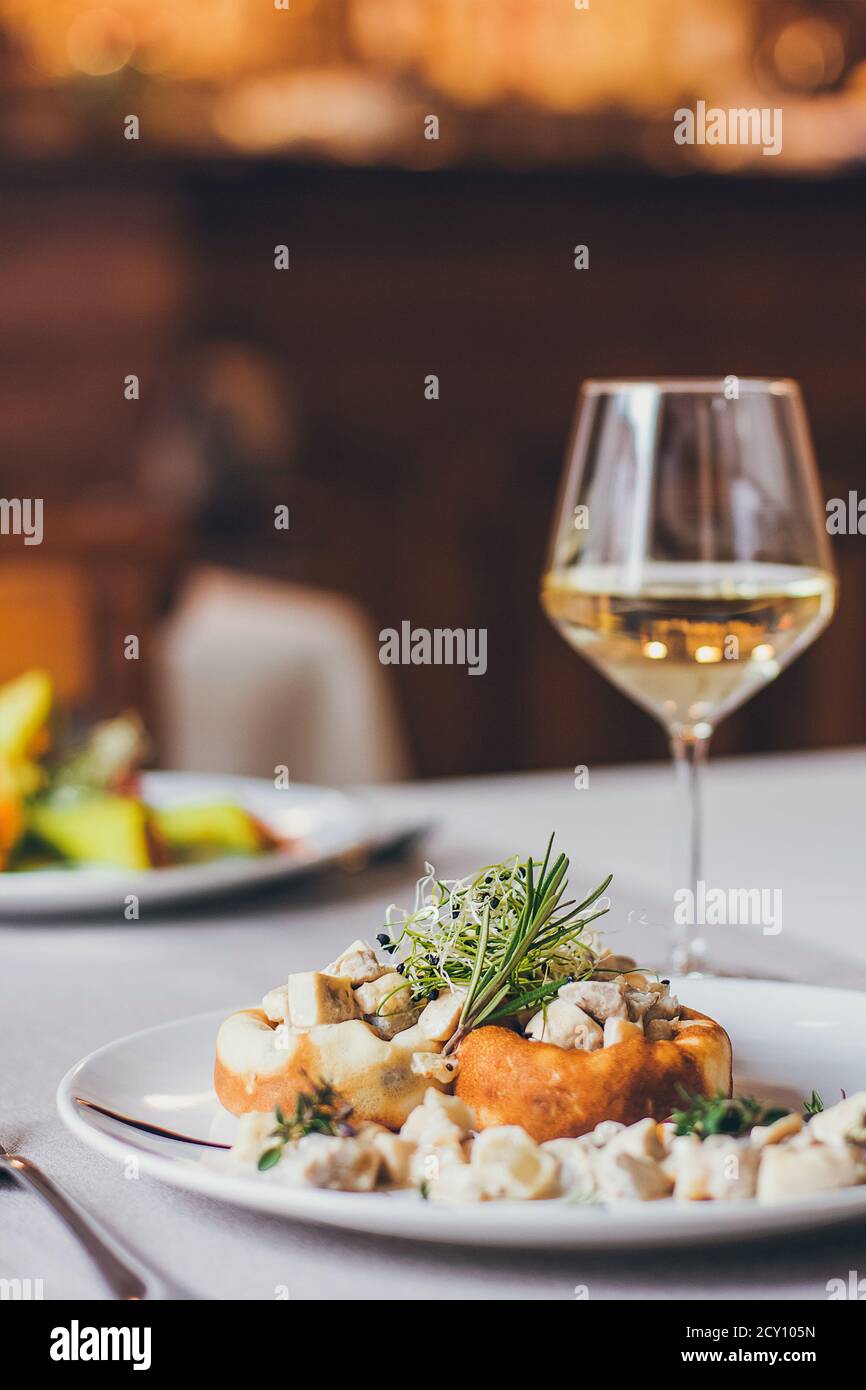 Stuffed mushrooms filled with cheese, mushroom stem and microgreen on the white plate with a glass of wine Stock Photo