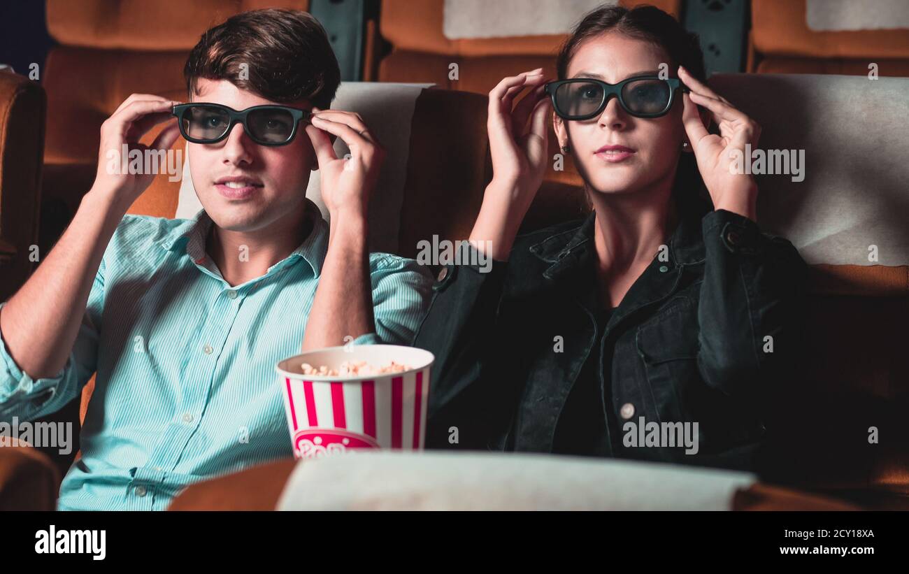 Man and woman in the cinema watching a movie with 3D glasses. with interest looking at the screen, exciting and eating popcorn Stock Photo
