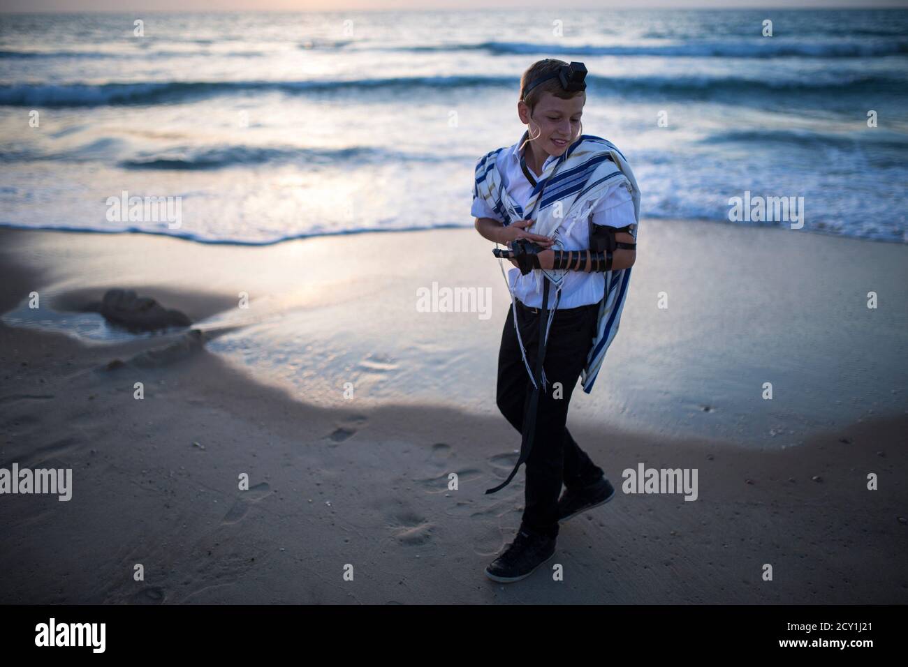 A Jewish boy wearing a prayer shawl and Tefillin, leather straps and boxes containing sacred parchments, has his Bar Mitzvah photographs taken on the shores of the Mediterranean Sea at Nitzanim beach, near the Israeli southern city of Ashkelon April 22, 2014.REUTERS/Amir Cohen (ISRAEL - Tags: SOCIETY RELIGION TPX IMAGES OF THE DAY) Stock Photo