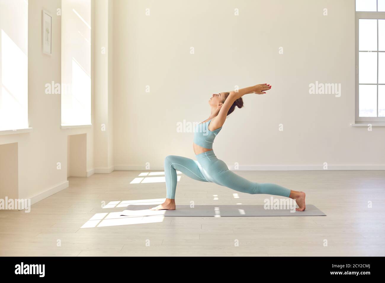 Beautiful young woman in activewear doing Crescent Lunge asana while practicing yoga in gym Stock Photo