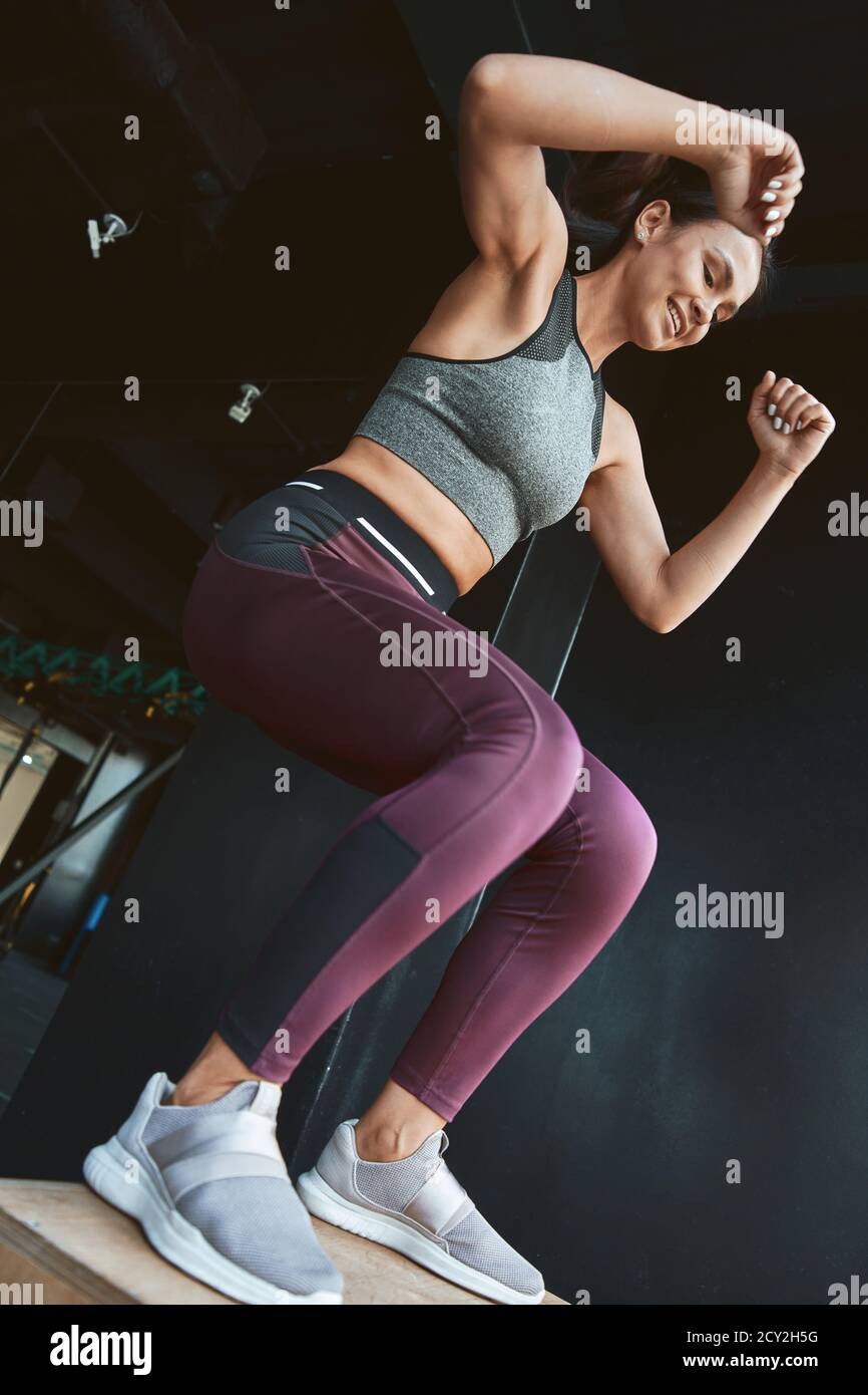 Best calorie burning Exercises. Bottom view of a strong athletic woman in sportswear doing box jump while working out at industrial gym, vertical shot. Sport, wellness and healthy lifestyle Stock Photo