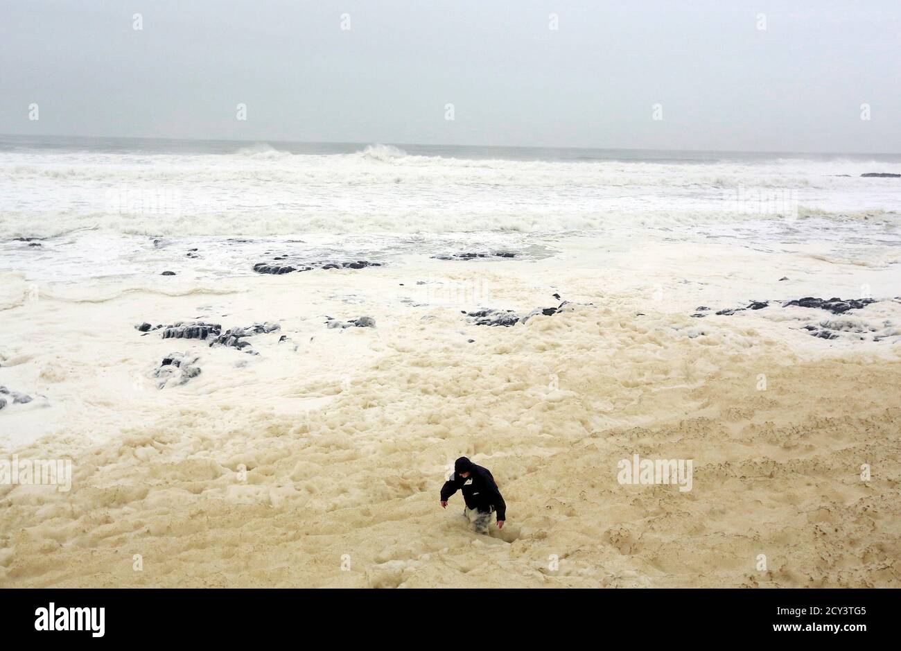 A man walks through sea foam created by storms, in the town of Portstewart on the Irish Coast January 9, 2015. The foam, known as spume, is caused by dissolved organic matter being agitated by breaking waves next to the shore.  REUTERS/Cathal McNaughton (NORTHERN IRELAND - Tags: ENVIRONMENT SOCIETY) Stock Photo