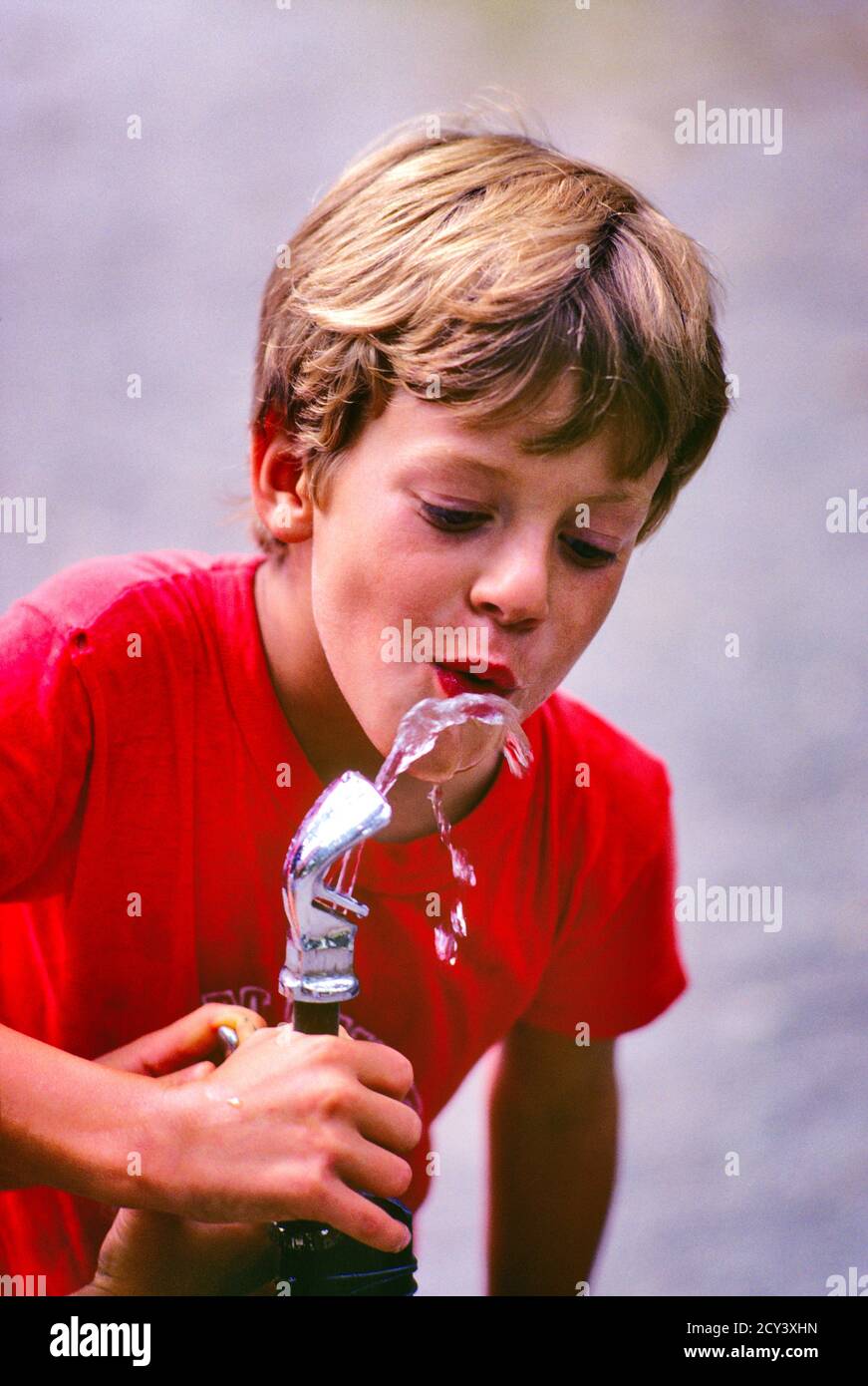 1970s THIRSTY BLOND PRETEEN BOY WEARING RED T-SHIRT REHYDRATING DRINKING COOL CLEAN SAFE REFRESHING WATER FROM OUTDOOR FOUNTAIN - cj00884 CAM001 HARS BLOND COOL SECURITY SAFETY PLEASED JOY LIFESTYLE HEALTHINESS COPY SPACE HALF-LENGTH MALES RISK EXPRESSIONS HAPPINESS WELLNESS CHEERFUL PROTECTION EXTERIOR RECREATION CAM001 PRETEEN SMILES CONCEPTUAL HYDRATION JOYFUL T-SHIRT JUVENILES PRE-TEEN PRE-TEEN BOY REFRESHING RELAXATION THIRSTY CAUCASIAN ETHNICITY OLD FASHIONED Stock Photo