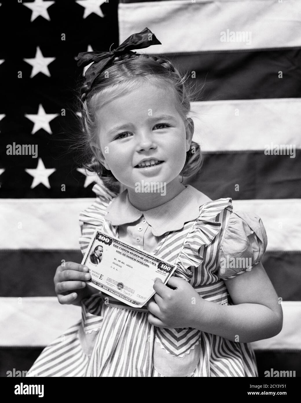 1940s WW2 SAVINGS BOND DRIVE SMILING APPEALING GIRL LOOKING AT CAMERA HOLDING $100 UNITES STATES SERIES E AMERICAN FLAG IN B/G - d2025 HAR001 HARS HISTORY CONFLICT FEMALES WW2 STUDIO SHOT RURAL HALF-LENGTH INSPIRATION CARING RISK CONFIDENCE B&W BOND EYE CONTACT FREEDOM SUCCESS HOME FRONT CHEERFUL STRENGTH VICTORY STRATEGY CHOICE EFFORT POWERFUL WORLD WARS PRIDE WORLD WAR WORLD WAR TWO WORLD WAR II IN OPPORTUNITY POLITICS SMILES CONCEPTUAL JOYFUL SUPPORT WORLD WAR 2 $100 E JUVENILES SERIES APPEALING BLACK AND WHITE CAUCASIAN ETHNICITY HAR001 OLD FASHIONED Stock Photo