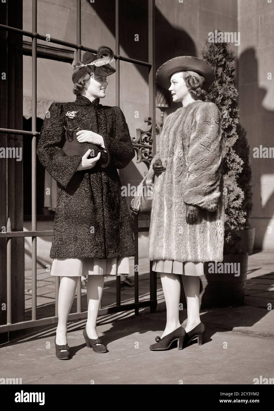 1930s 1940s TWO FASHIONABLE WOMEN WEARING HATS FUR COATS GLOVES STANDING MEETING TALKING TOGETHER SHOPPING OUTSIDE UPSCALE STORE - f4234 HAR001 HARS COMMUNICATION YOUNG ADULT WEALTHY FASHIONABLE RICH LIFESTYLE FEMALES COATS LUXURY COPY SPACE FRIENDSHIP FULL-LENGTH LADIES PERSONS CONFIDENCE B&W HANDBAGS BUZZ HAPPINESS STYLES BUSYBODY PRIDE TELLING STORIES UPSCALE CONCEPTUAL AFFLUENT STYLISH TATTLER HEARSAY CHINCHILLA FASHIONS MID-ADULT MID-ADULT WOMAN RUMORS TOGETHERNESS WELL-TO-DO YOUNG ADULT WOMAN BLACK AND WHITE CAUCASIAN ETHNICITY HAR001 HIGH HEELS OLD FASHIONED PERSIAN LAMB Stock Photo
