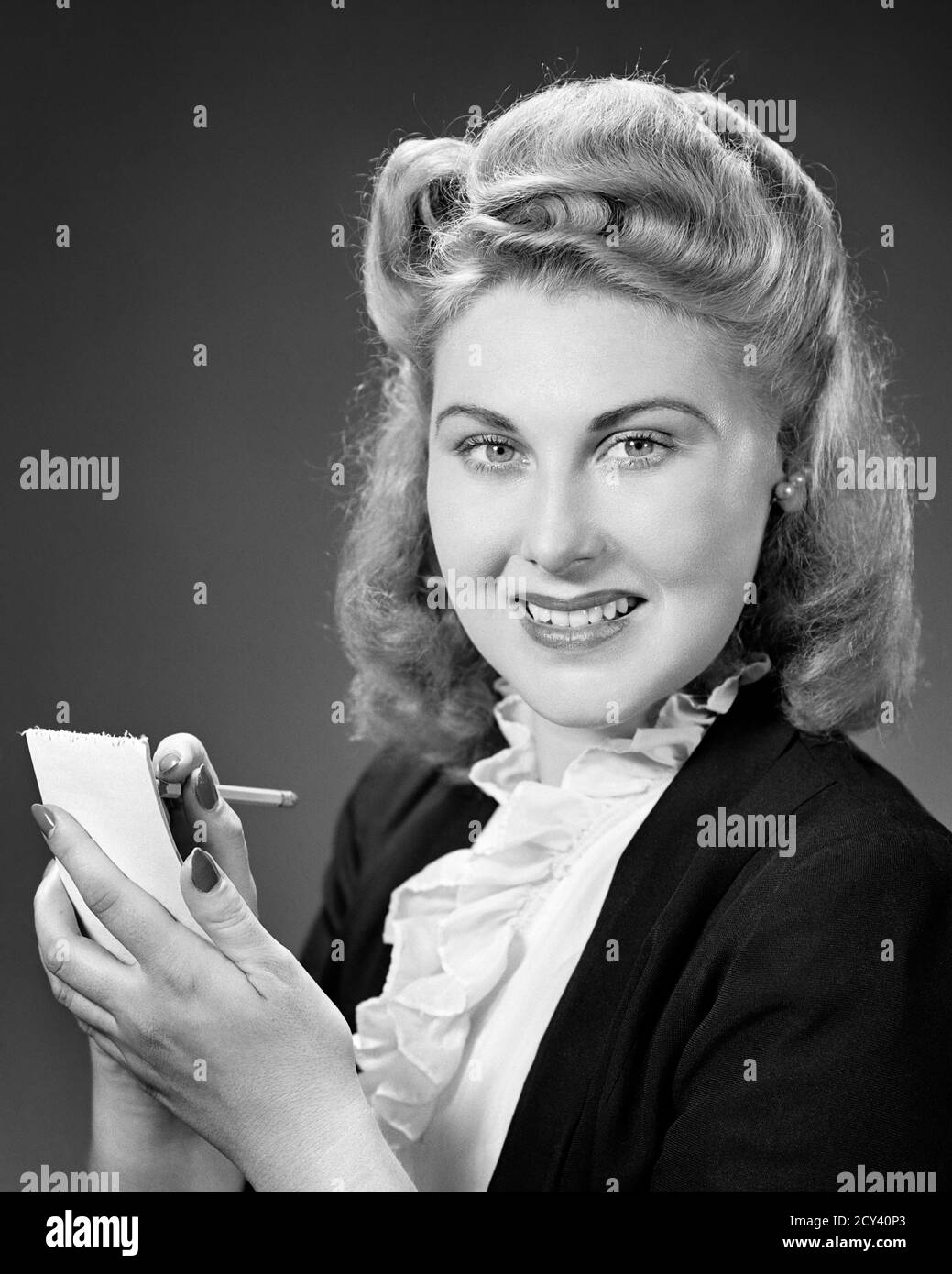 1940s SMILING BLOND WOMAN WITH VERY BIG VICTORY ROLLS HAIR STYLE RUFFLE  SHIRT LOOKING AT CAMERA WRITING ON NOTEPAD WITH PENCIL - g25 HAR001 HARS  FEMALES WINNING COPY SPACE LADIES PERSONS RECORDING