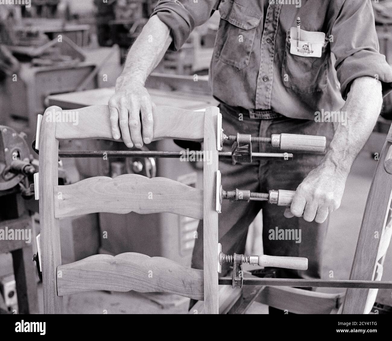 1960s MAN CRAFTSMAN HANDS BUILDING MAKING REFINISHING FURNITURE USING WOODWORKING SCREW TIGHTEN CLAMPS GLUING UP CHAIR BACK - i5560 HAR001 HARS SKILL OCCUPATION SKILLS STRENGTH CUSTOMER SERVICE CAREERS KNOWLEDGE PROGRESS LABOR PRIDE UP EMPLOYMENT MANUFACTURING OCCUPATIONS USING REPAIRING CONCEPT CONCEPTUAL CLOSE-UP KIND EMPLOYEE SYMBOLIC WOODWORKING CLAMPS CONCEPTS CRAFTSMAN CREATIVITY GLUING MANUFACTURE MID-ADULT MID-ADULT MAN PRECISION REFINISHING SCREW BLACK AND WHITE CAUCASIAN ETHNICITY HANDS ONLY HAR001 LABORING OLD FASHIONED REPRESENTATION VISE Stock Photo