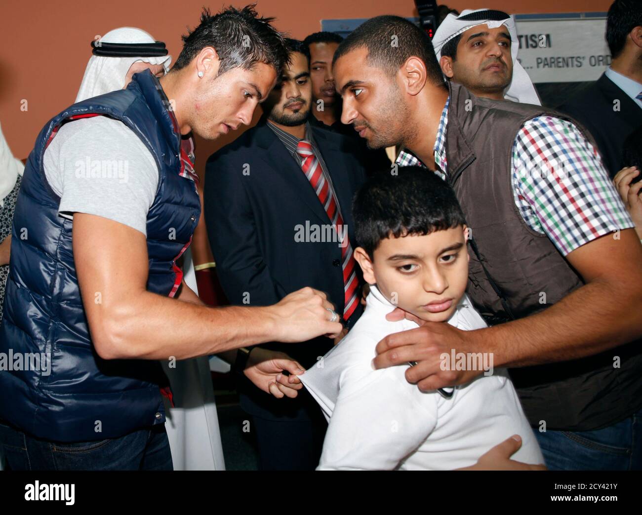 Real Madrid's Cristiano Ronaldo (L) sings an autistic boy's t-shirt during  his visit to the Autism centre in Dubai December 28, 2011. REUTERS/Ahmed  Jadallah (UNITED ARAB EMIRATES - Tags: SPORT ENTERTAINMENT Stock