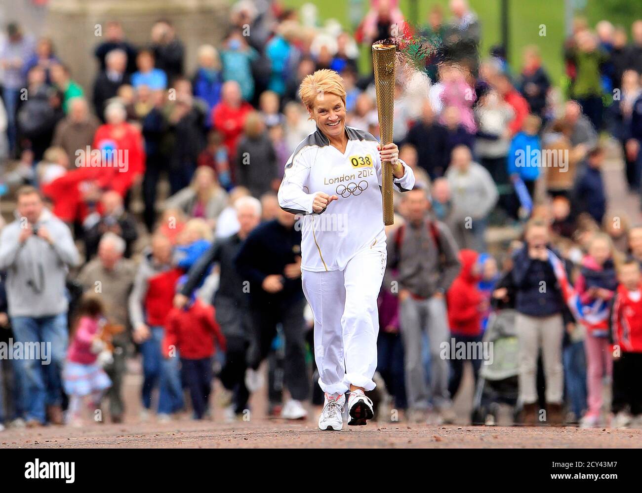 Geraldine McCann carries the Olympic torch towards Parliament Buildings in Belfast June 3, 2012. On Sunday the Olympic flame - on a five-day visit to Northern Ireland - will be carried to the Titanic Building, recently opened in Belfast's docklands to commemorate the famous liner which was built in the city and sank 100 years ago. It will then make its way through more than 60 towns and villages across Northern Ireland, carried by about 600 local people aged between 12 to 93.   REUTERS/Cathal McNaughton (NORTHERN IRELAND - Tags: SPORT OLYMPICS SOCIETY) Stock Photo