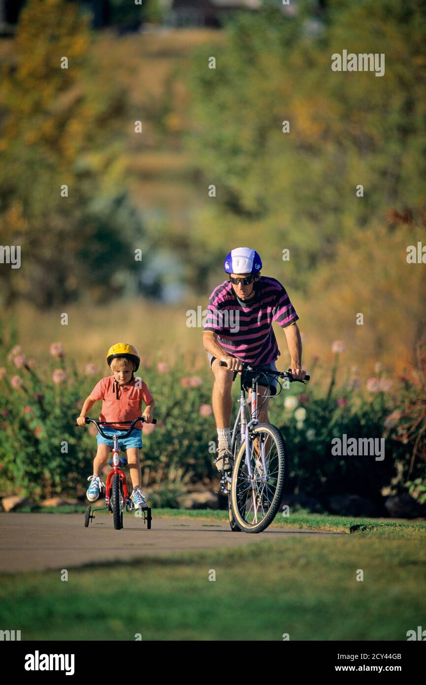 1990s FATHER AND CHILD WEARING HELMETS AND RIDING BIKES BOY ON BIKE WITH  TRAINING WHEELS ATTACHED - kb30180 WAL004 HARS OLD FASHION 1 DRIVEWAY  FITNESS JUVENILE HEALTHY YOUNG ADULT SAFETY SONS FAMILIES