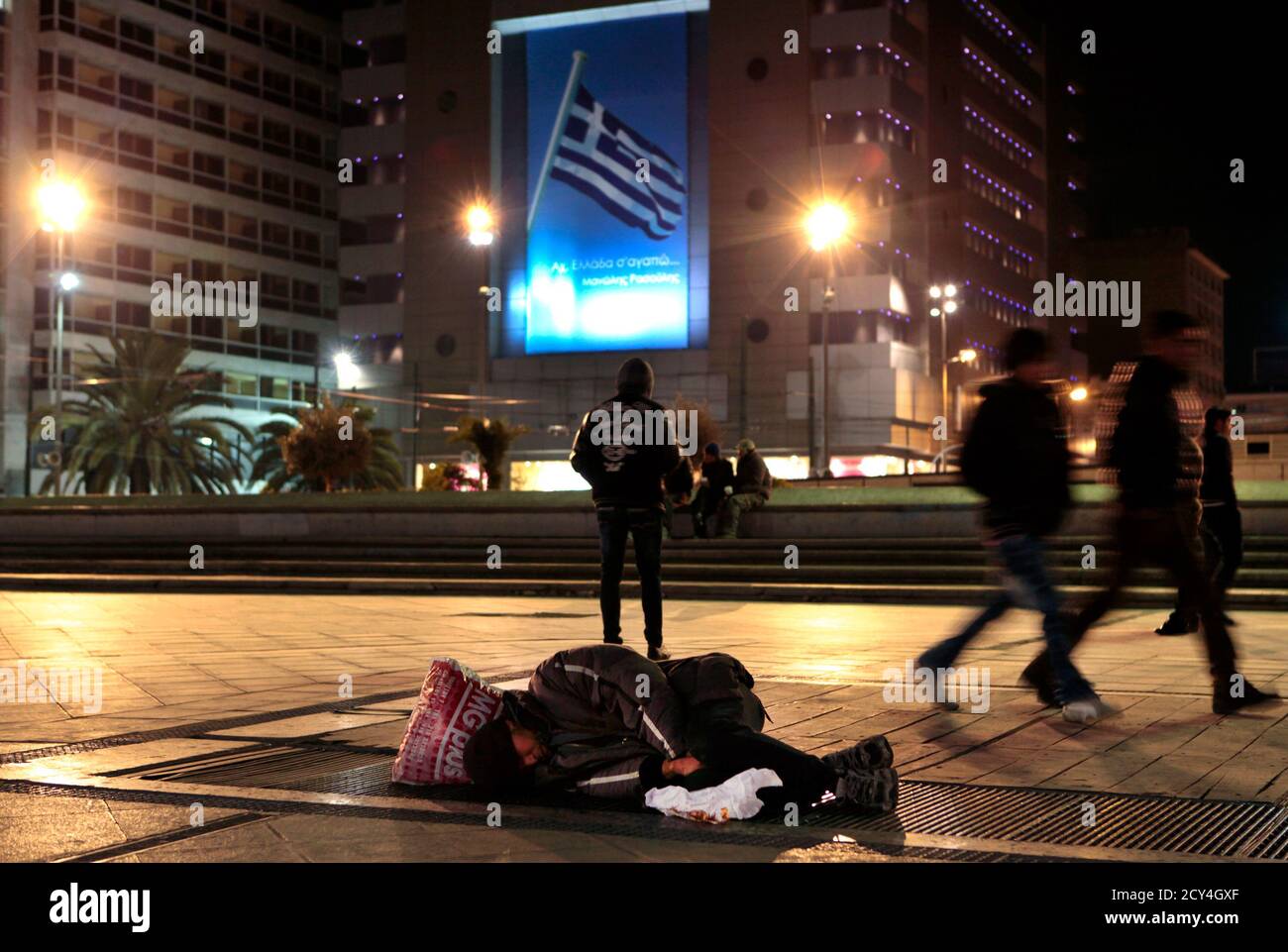 A homeless man sleeps on Metro vents in Omonia square in central Athens by a huge poster featuring a Greek flag and the words A homeless man sleeps on Metro vents in Omonia square in central Athens by a huge poster featuring a Greek flag and the words