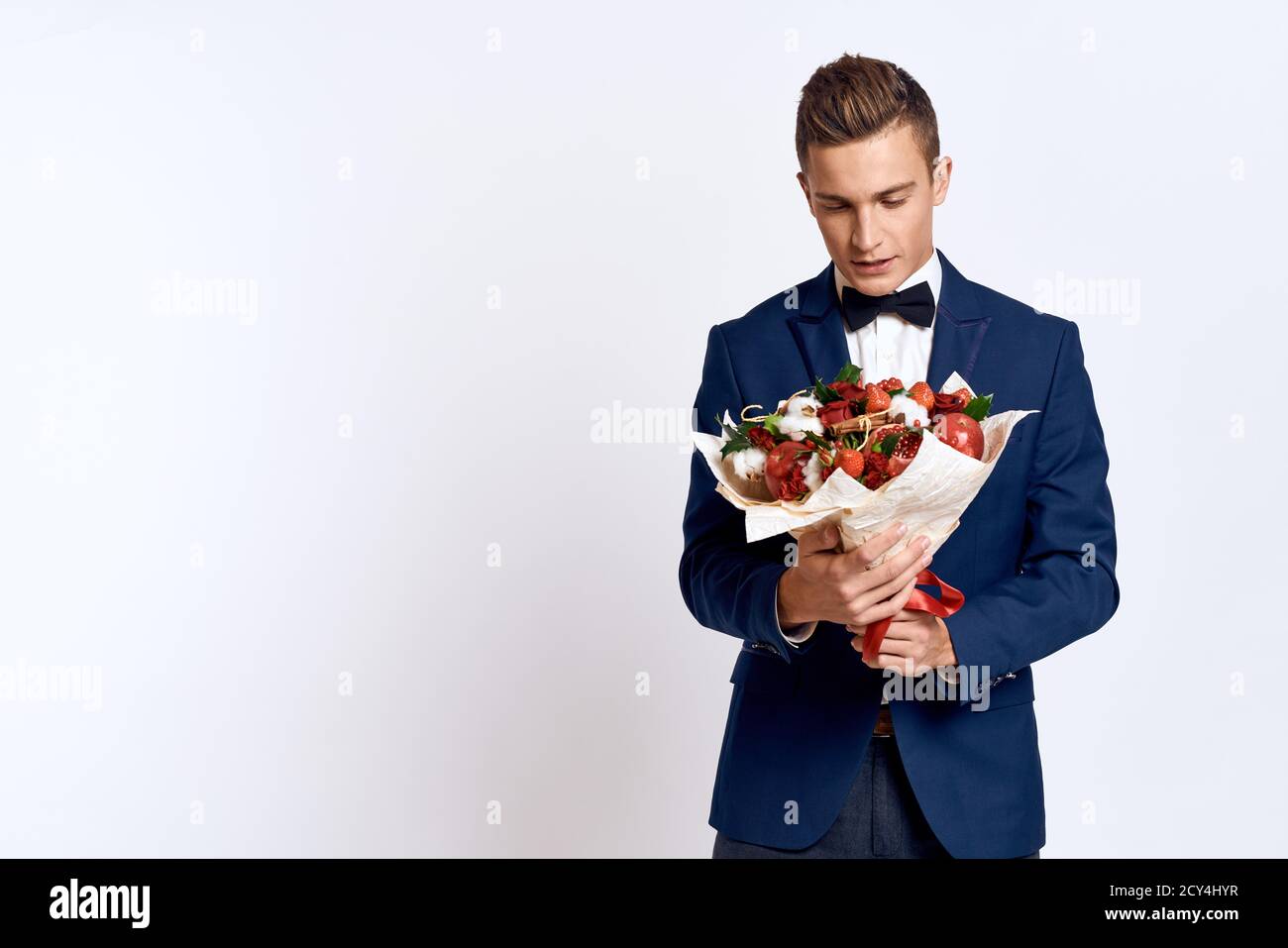 An elegant man in a classic suit with a bow tie holds a bouquet of ...