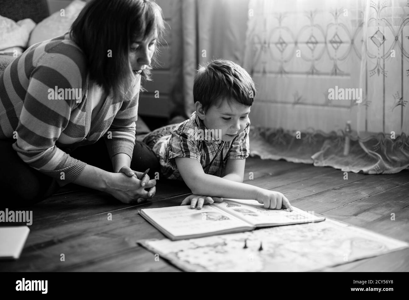 Woman reading a book with her little son sitting on the floor in home. Black and white photo. Stock Photo
