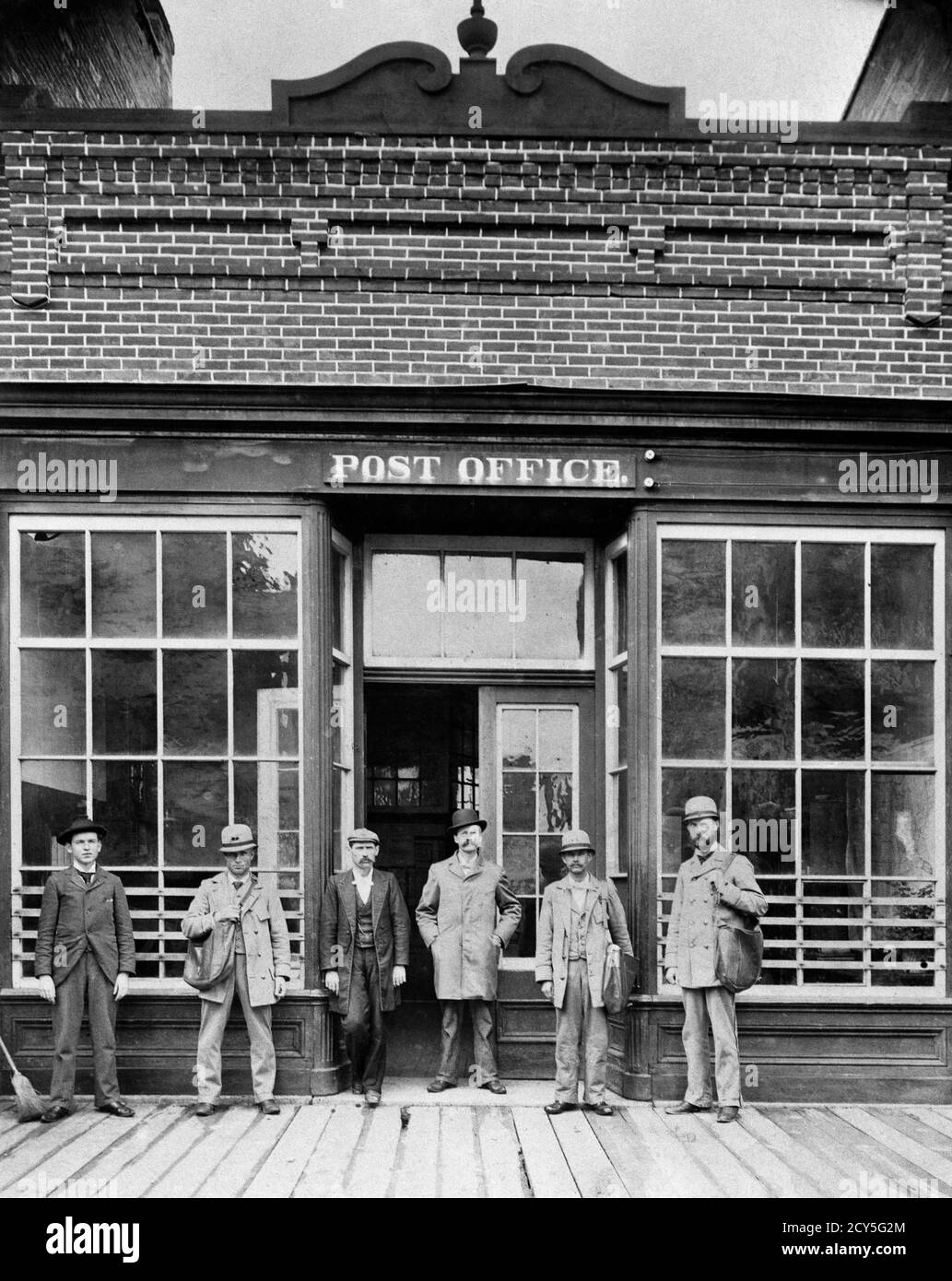 1900s 1910s TURN OF THE 20TH CENTURY GROUP OF UNIFORMED MEN POSTMEN CARRYING LEATHER MAIL BAGS IN FRONT OF POST OFFICE BUILDING - o3415 LEF001 HARS DOORS DOORWAY MAIL OLD TIME POSTMAN NOSTALGIA INDUSTRY OLD FASHION MANY COMMUNICATION TEAMWORK SUITS TURN WORKMAN LINED LIFESTYLE HISTORY ARCHITECTURE VERTICAL GROWNUP 6 UNITED STATES COPY SPACE FULL-LENGTH PERSONS POSTAL UNITED STATES OF AMERICA MALES SIX BUILDINGS DOORWAYS B&W GOVERNMENT WINDOWS NORTH AMERICA EYE CONTACT NORTH AMERICAN OFFICES STRUCTURE WORKMEN MANUAL PROPERTY CUSTOMER SERVICE TURN OF THE 20TH CENTURY WORKFORCE Stock Photo