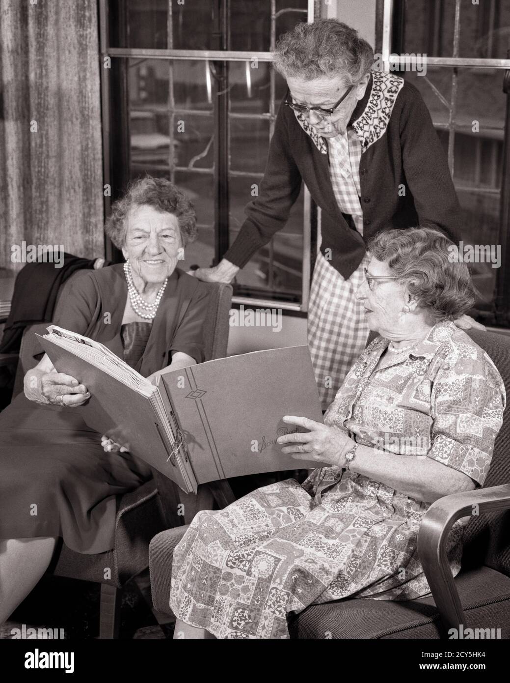 1960s THREE SENIOR WOMEN STANDING SITTING SIDE BY SIDE READING SHARING A MEMORY SCRAPBOOK PHOTO ALBUM IN RETIREMENT HOME - s15919 HAR001 HARS COMMUNICATION FRIEND PLEASED FAMILIES JOY LIFESTYLE MEMORY SATISFACTION ELDER FEMALES HOME LIFE SCRAPBOOK COPY SPACE FRIENDSHIP HALF-LENGTH LADIES PERSONS RETIREMENT SIBLINGS SISTERS SENIOR ADULT B&W SENIOR WOMAN RETIREE HAPPINESS OLD AGE OLDSTERS CHEERFUL OLDSTER LEISURE AGING EXCITEMENT REMEMBER PRIDE A IN SIBLING SMILES ELDERS CONNECTION CONCEPTUAL FRIENDLY JOYFUL AGISM COOPERATION ELDERLY WOMAN MEMORIES SIDE BY SIDE TOGETHERNESS BLACK AND WHITE Stock Photo