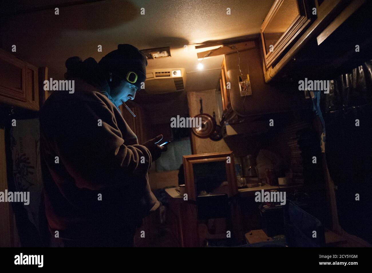 Bazileo Hernandez looks at his mobile phone in an RV parked on the streets of Williston, North Dakota January 13, 2015. A man offered to let Hernandez and his friends stay in the vehicle with him overnight since temperatures outside were below zero. The trio had arrived in town earlier that day with no jobs and nowhere to stay, but hoped to find work in the Bakken oil fields. Like so many before them, Terra Green, Jeff Williamson and Bazileo Hernandez came to North Dakota's oil country seeking a better life. They just came too late. Itinerant, unskilled workers could as recently as last spring Stock Photo