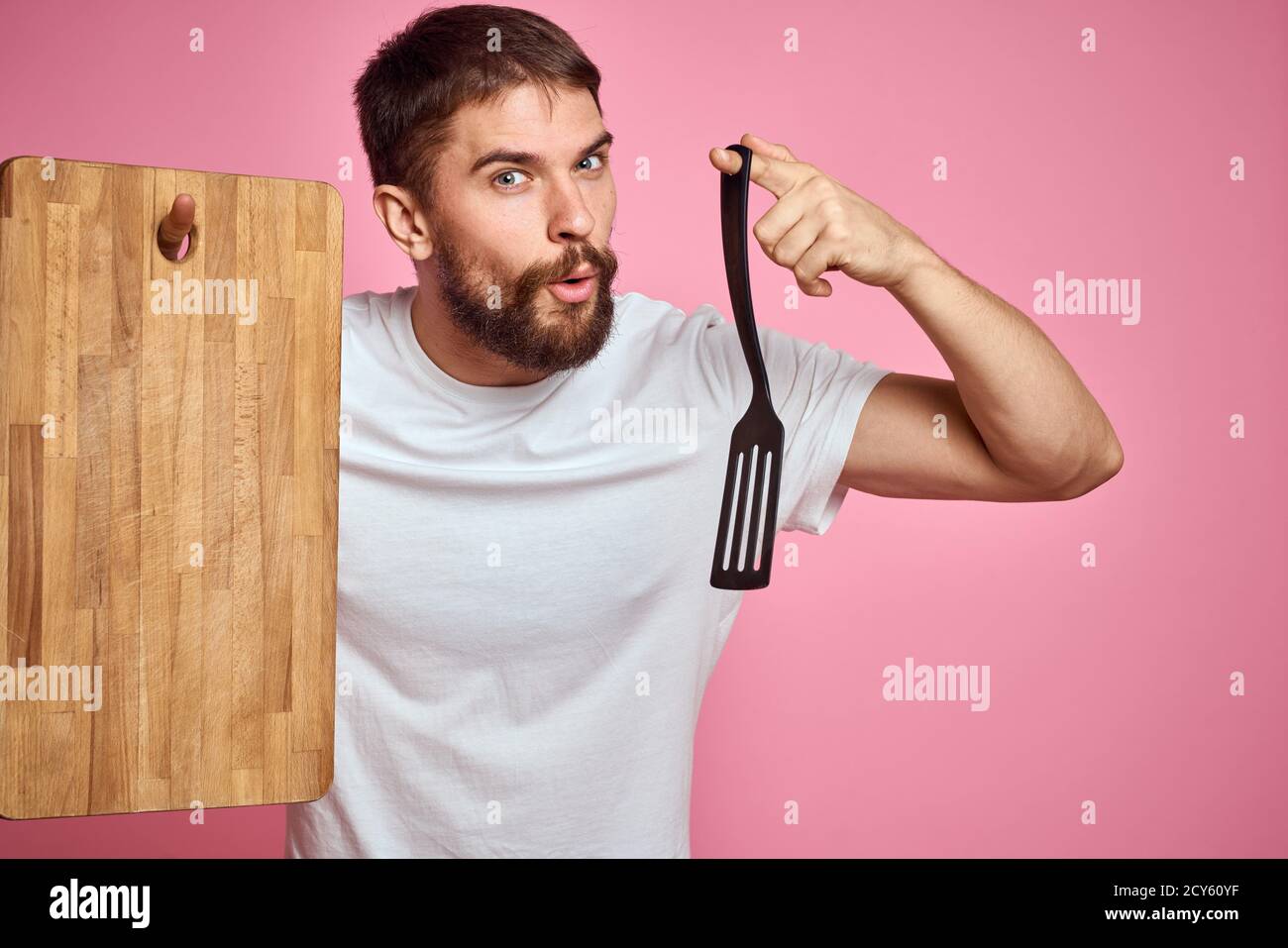 guy holding kitchen board and spatula in hand on pink background