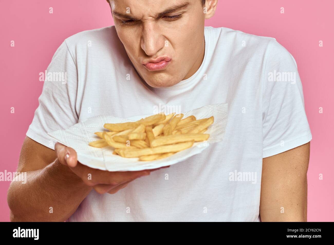 Man with French fries in a paper box on a pink background calories fast
