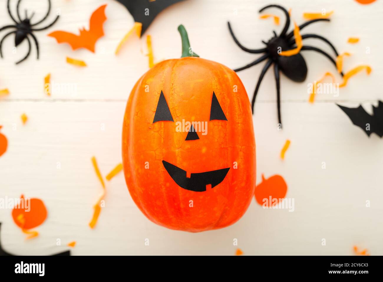 Halloween background with jack-o'-lanter, paper bats, spiders, confetti on white wooden background. Halloween holiday decorations. Flat lay, top view Stock Photo