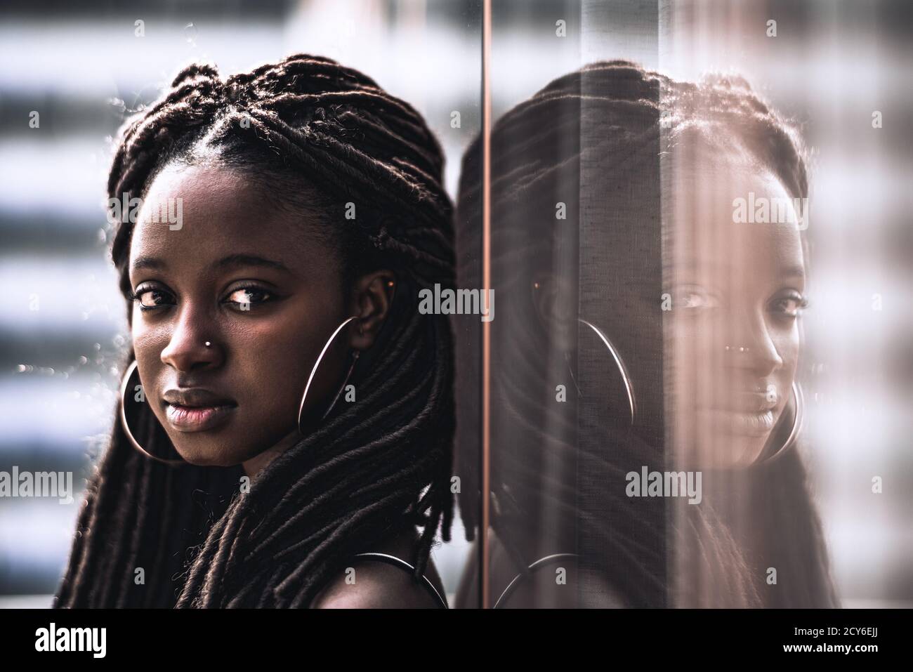 A portrait of a young dazzling African woman with big earrings, nose piercing, and beautiful dreadlocks, she is looking at the camera while leaning ag Stock Photo