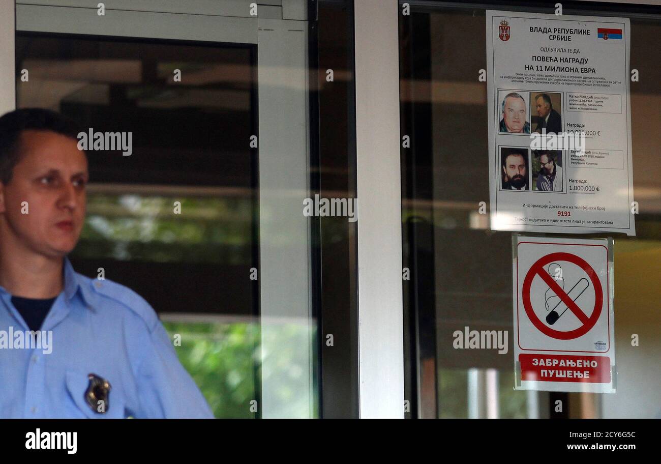 A security officer stands near a wanted poster of Bosnian Serb wartime  general Ratko Mladic at the entrance of the Special Court, where Mladic is  being held, in Belgrade May 30, 2011.