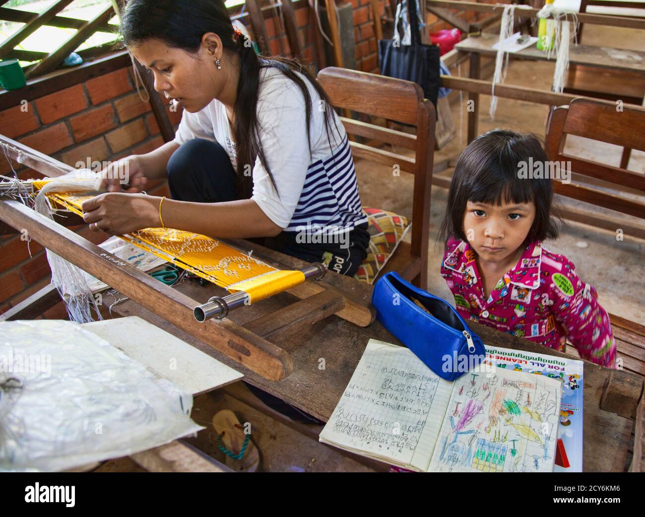 Angkor, Cambodia - Oct 11, 2911: Woman creating thread at a silk factory with her daughter studying nearby Stock Photo